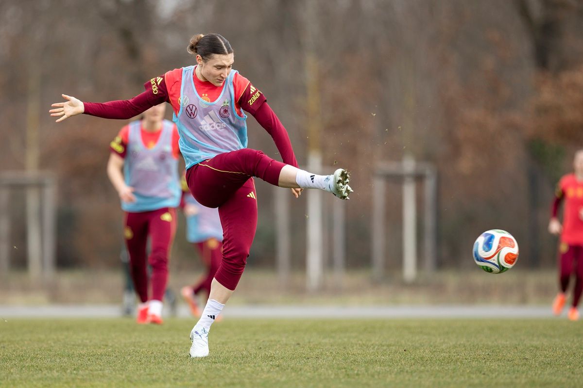 Eine Fußballspielerin in Trainingskleidung schießt einen Ball während des Trainings auf einem grünen Platz.