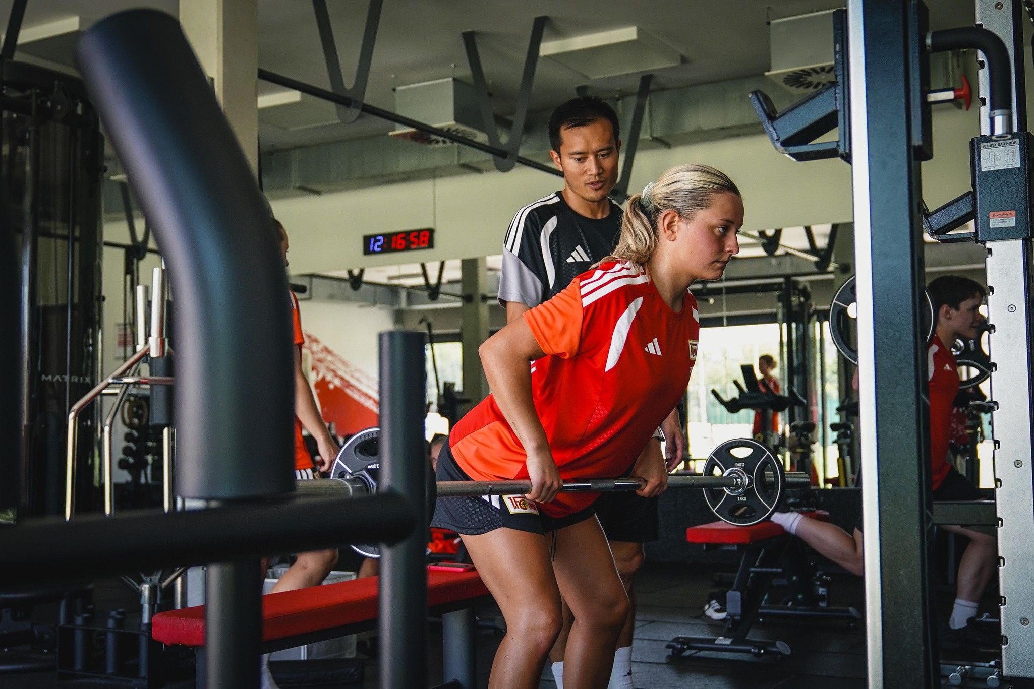 Eine Trainerin beobachtet eine Sportlerin beim Krafttraining im Fitnessstudio. Beide tragen Sportkleidung.