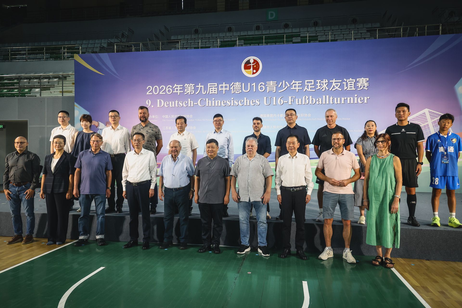 Gruppenfoto von Teilnehmern des Deutsch-Chinesischen U16-Fußballturniers 2026 auf einer Bühne in einer Sporthalle.