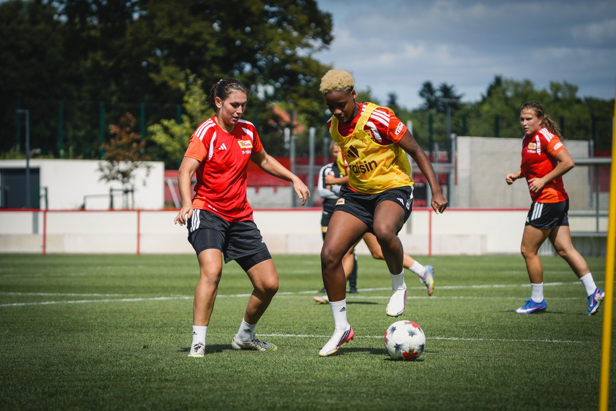 Zwei Fußballspielerinnen trainieren auf einem grünen Platz, während eine von ihnen den Ball dribbelt.