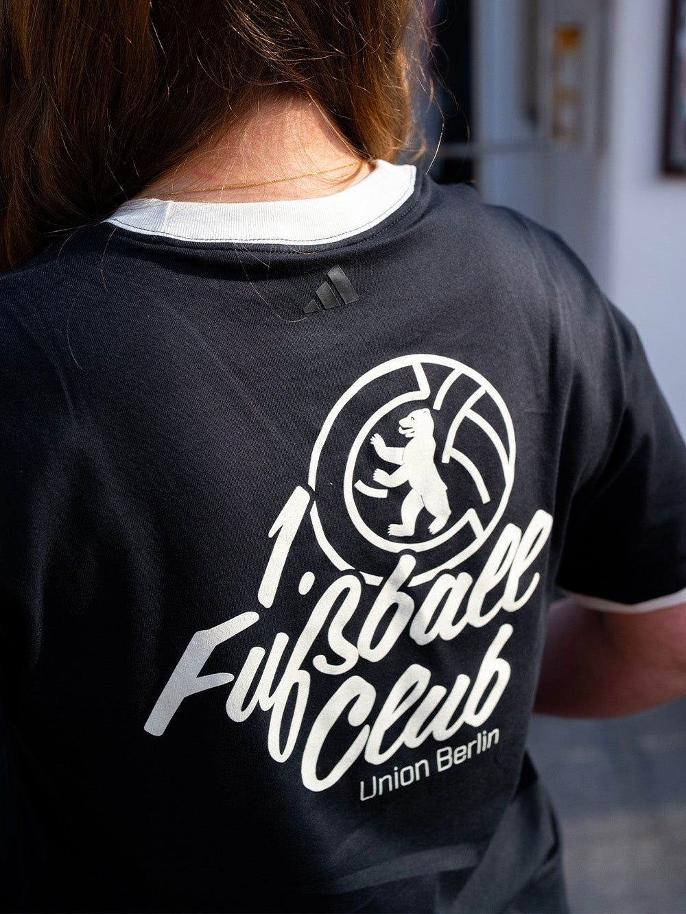 Rückansicht eines schwarzen T-Shirts mit dem Aufdruck „1. Fußball Club Union Berlin“ und dem Adidas-Logo.