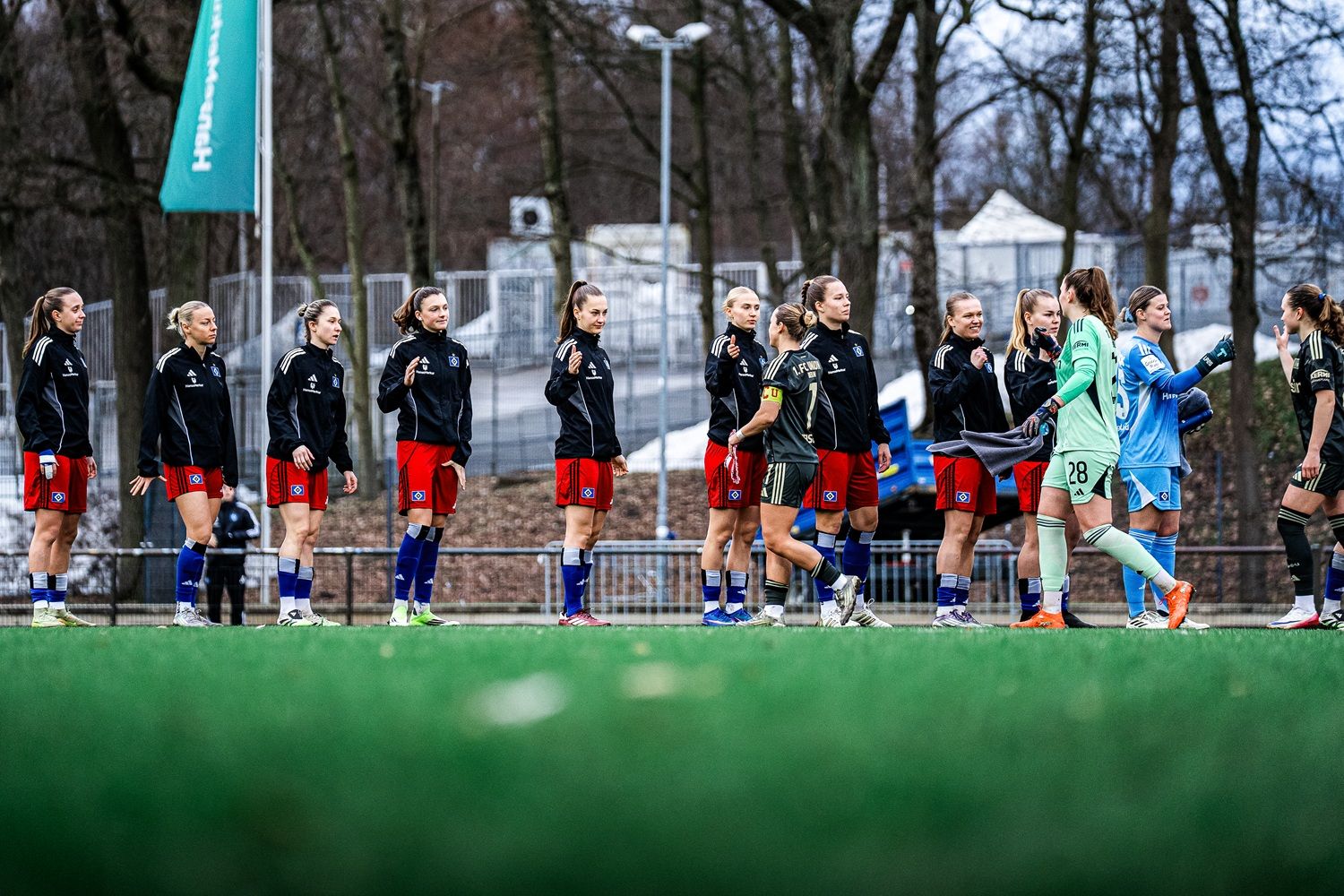 Fußballspielerinnen in Trainingkleidung applaudieren sich gegenseitig auf einem Sportplatz im Freien.