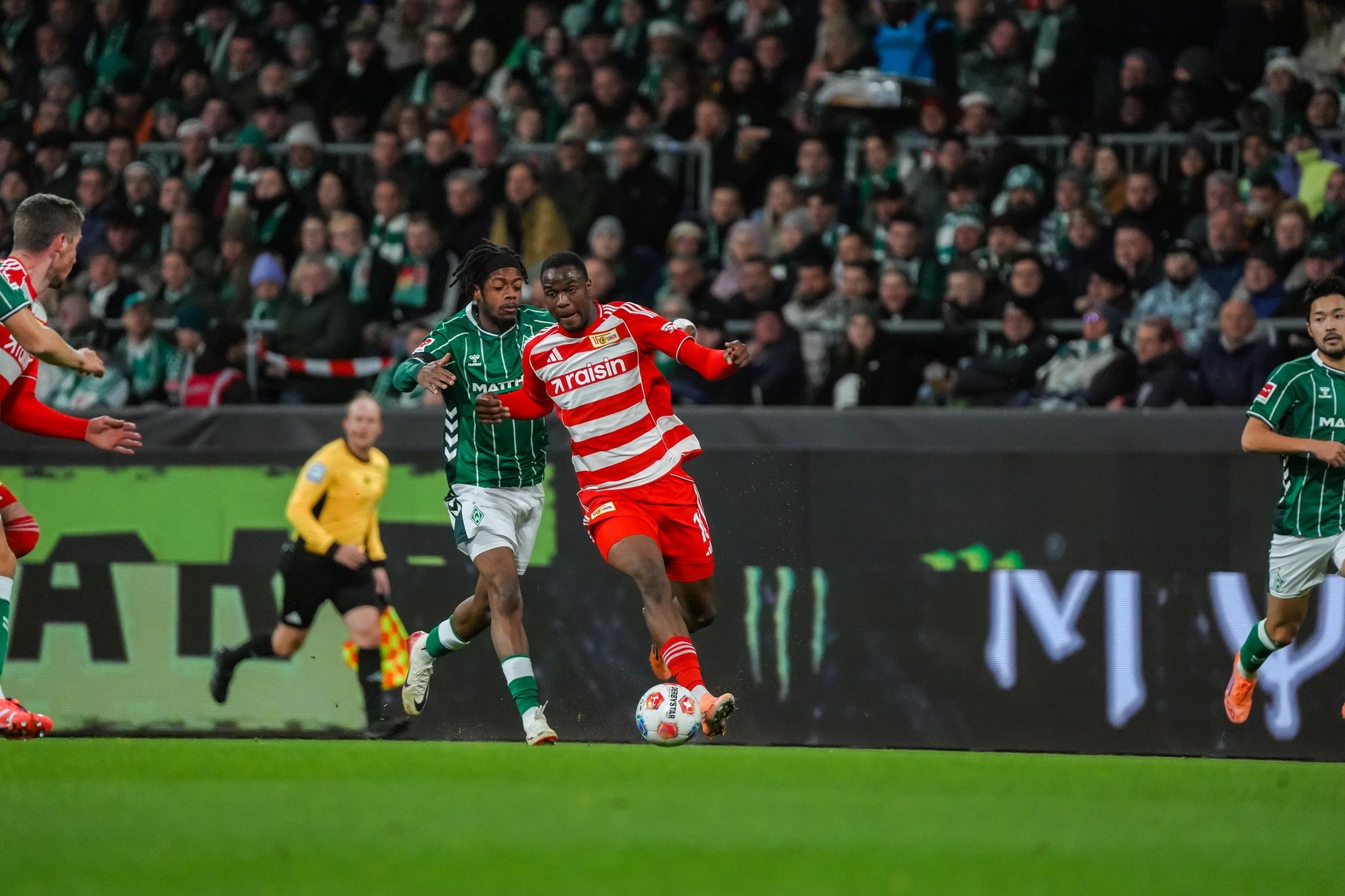 Two soccer players competing for the ball during a game, with cheering fans in the background.