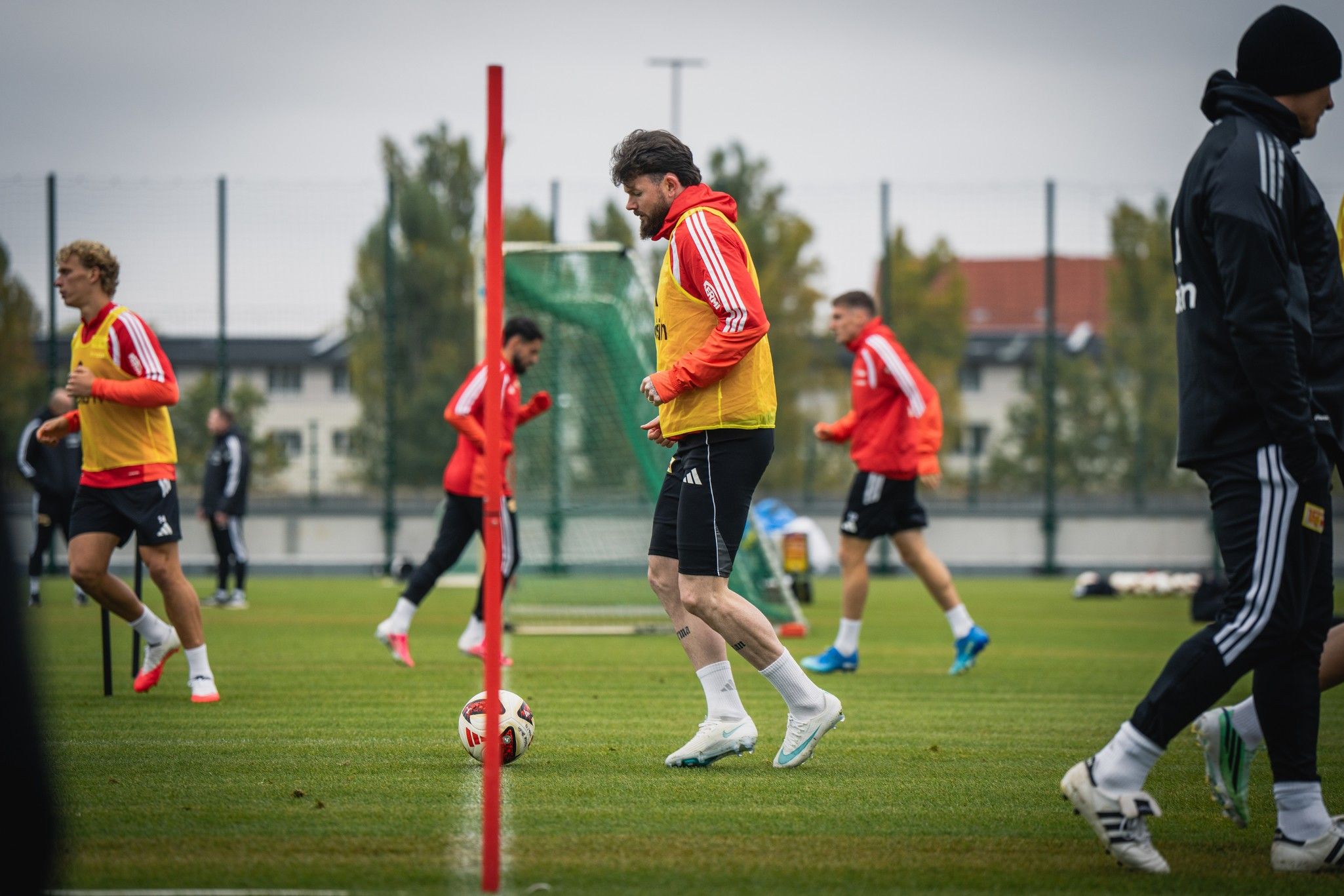 Fußballtraining auf einem grünen Platz mit Spielern in roten und schwarzen Trikots, die an einer Übung teilnehmen.