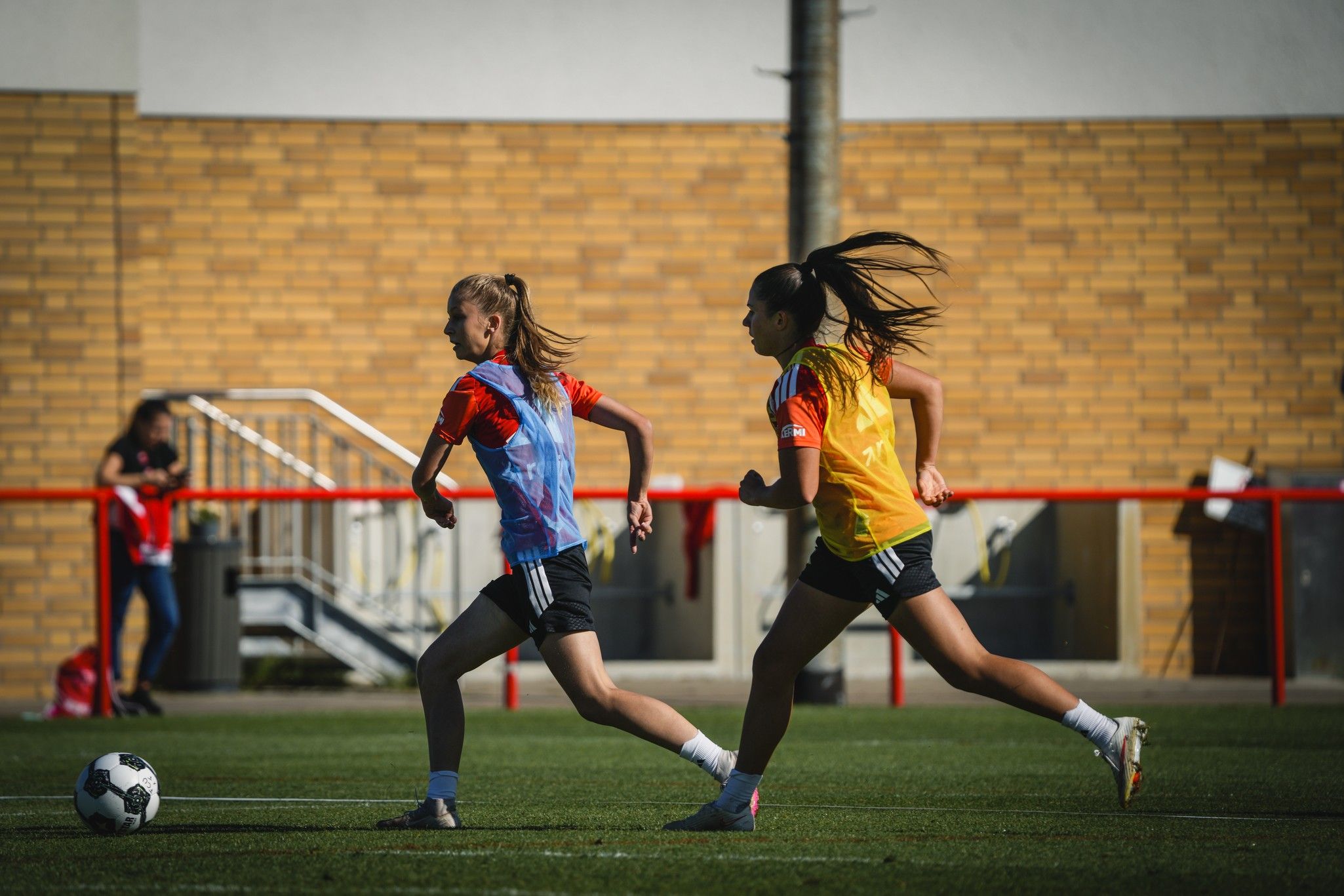 Zwei Fußballspielerinnen sprinten auf einem Trainingsfeld in Sportkleidung.