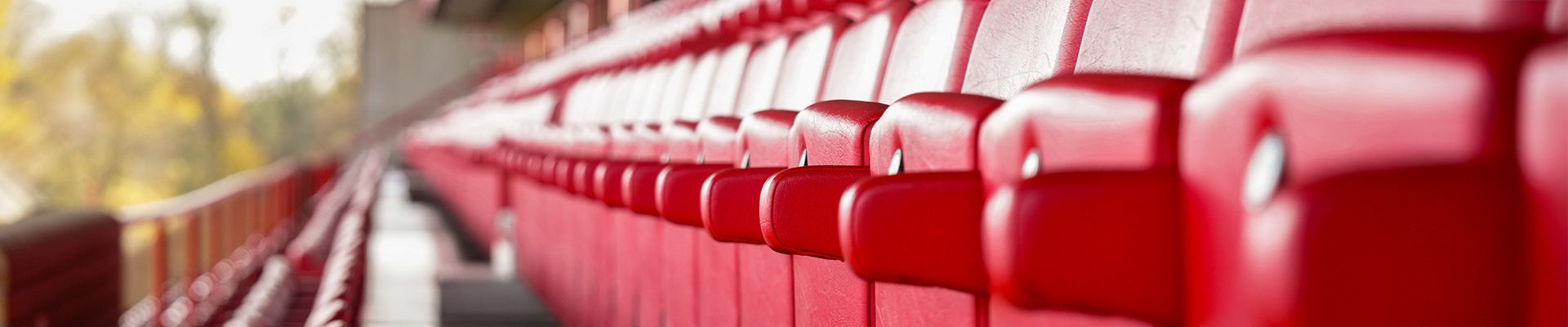 Rote Stadionplätze in einer Reihe, mit unscharfem Hintergrund und natürlichem Licht.