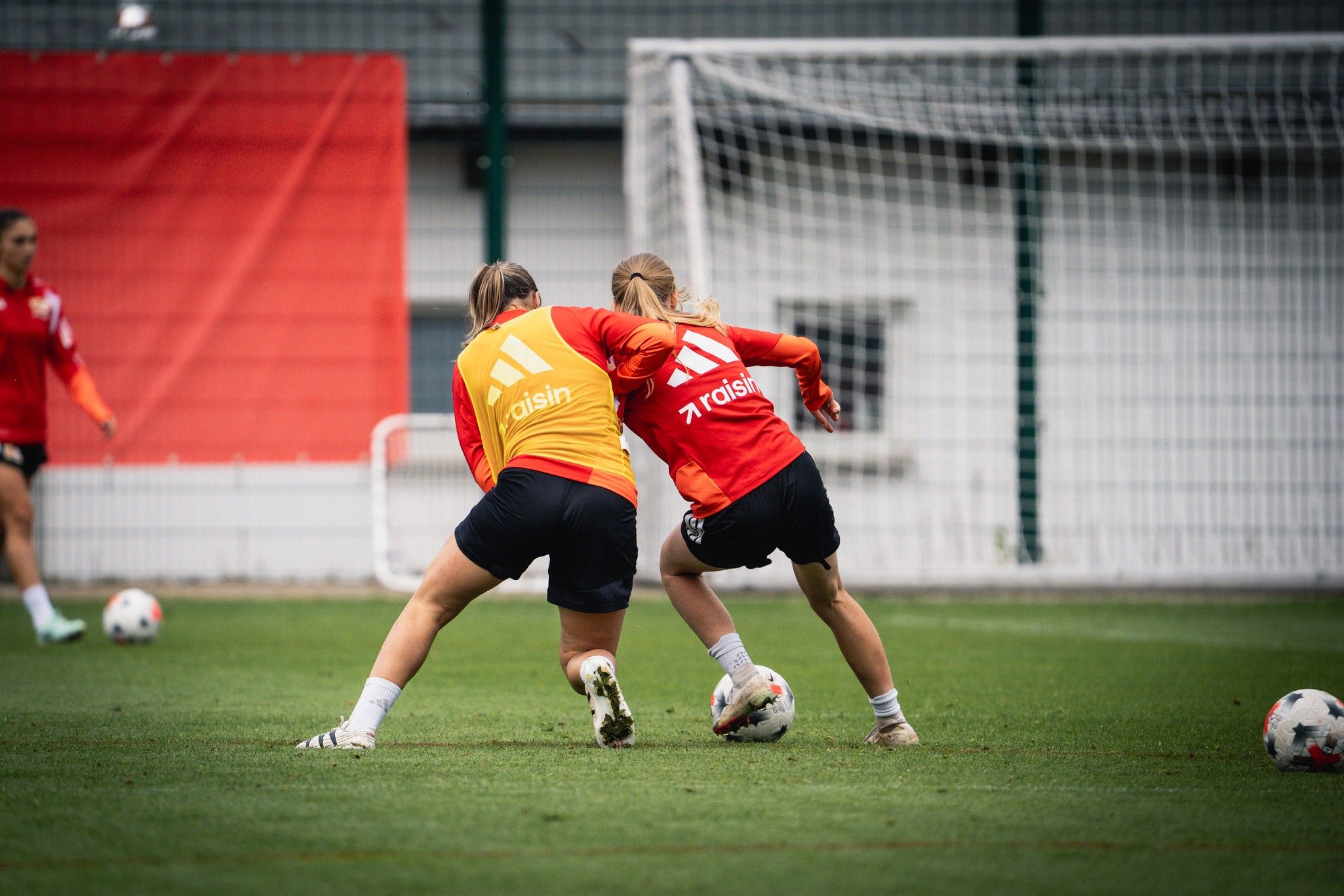 Zwei Fußballspielerinnen in Training, die im Wettkampf um den Ball miteinander ringen, auf einem Rasenplatz.
