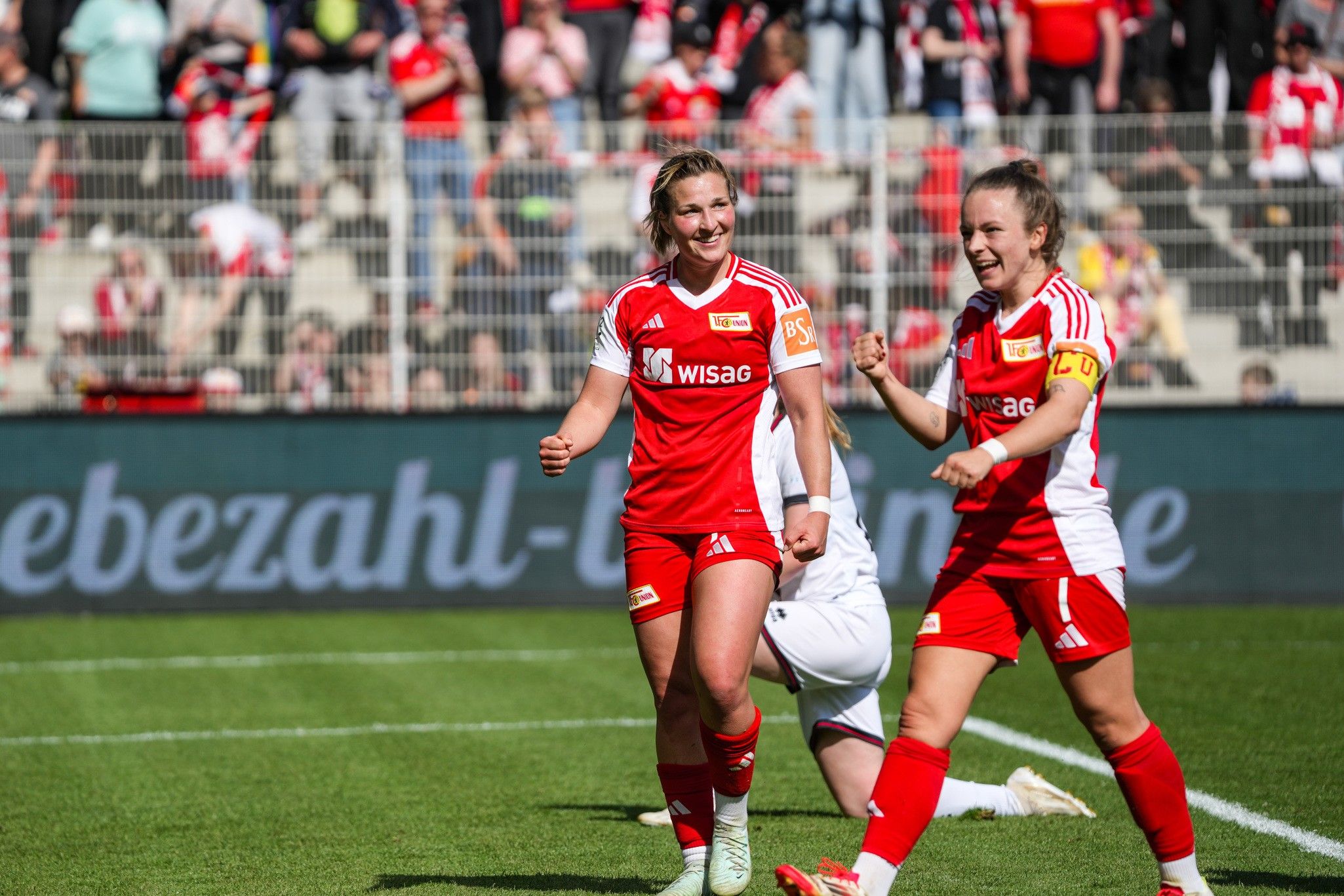Zwei Spielerinnen des 1. FC Union Berlin jubeln über ein Tor im Stadion, im Hintergrund stehen viele Zuschauer.