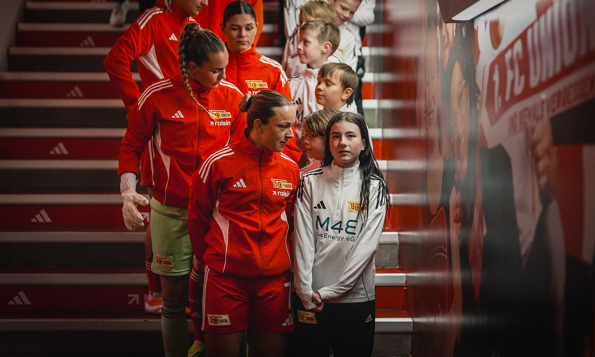 Fußballmannschaft in roten Trikots geht die Treppe hinunter, begleitet von Kindern, die sie anfeuern.