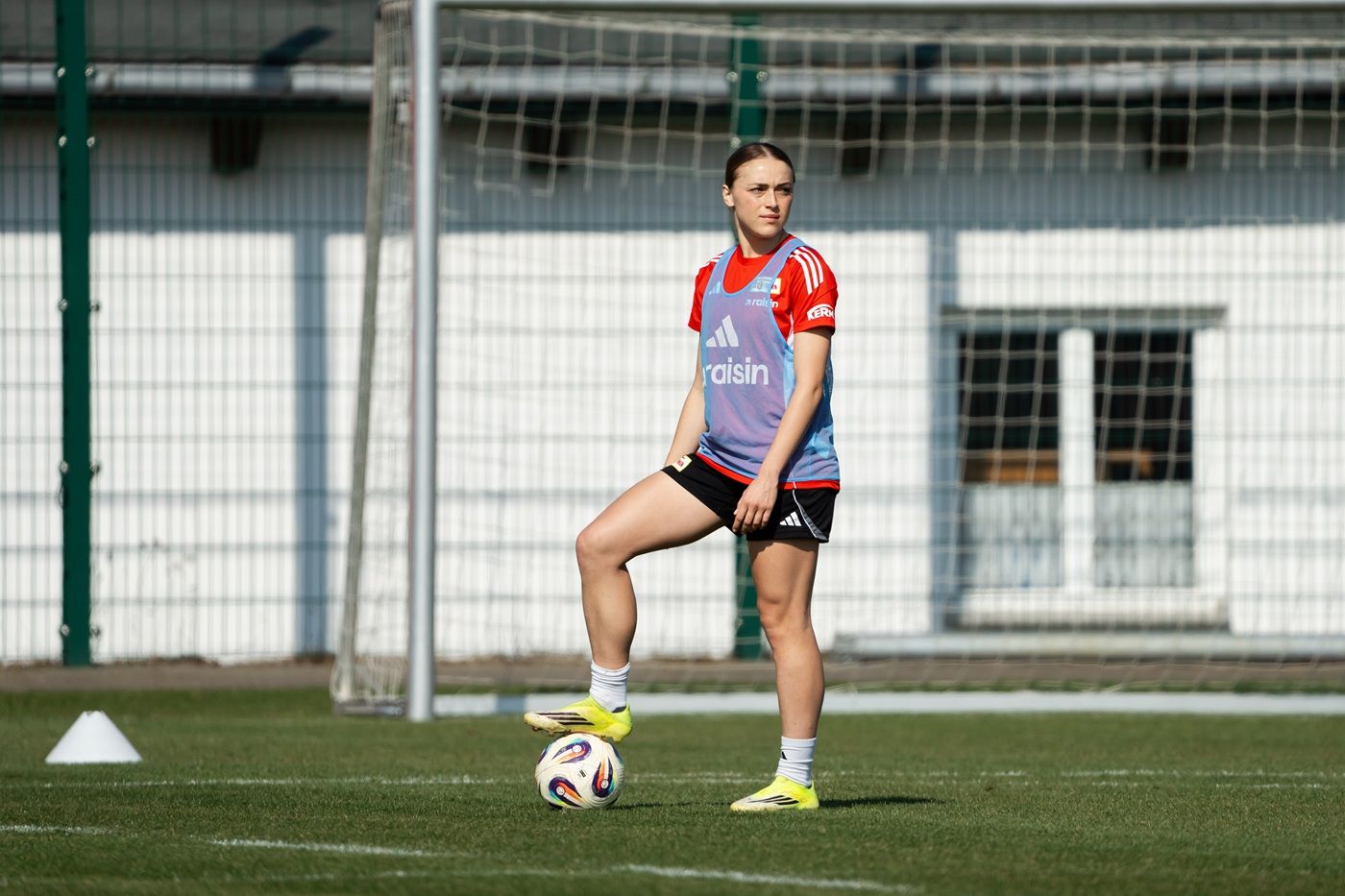 Eine Fußballspielerin steht in Trainingskleidung neben einem Ball auf dem Spielfeld.