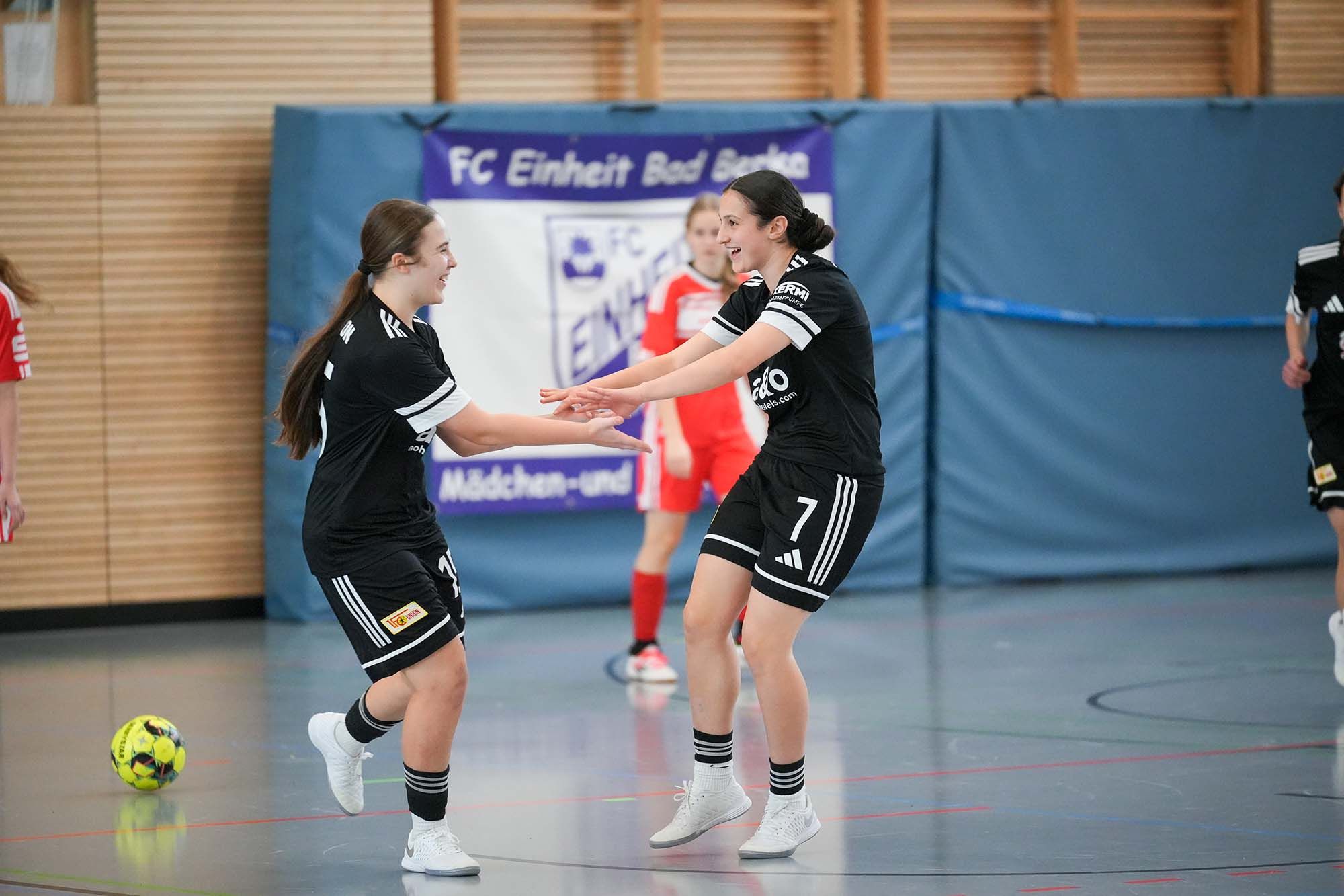 Zwei Mädchen in schwarzen Trikots feiern nach einem Spiel im Hallenfußball in einer Sporthalle.