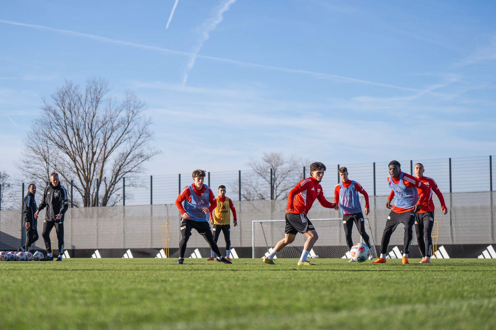 Spielende Fußballspieler in roten Trikots trainieren auf einem grünen Rasenplatz an einem sonnigen Tag.