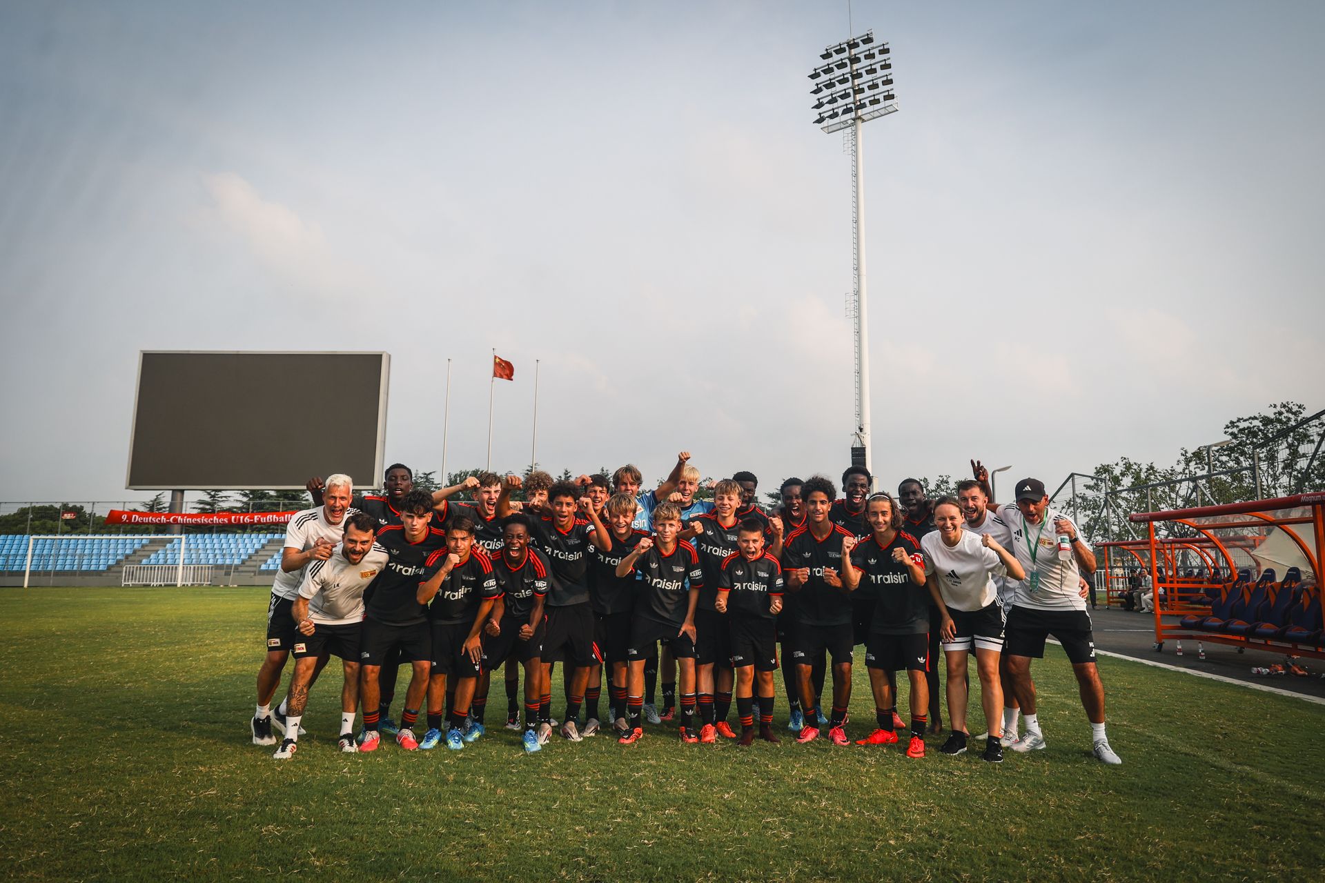 Eine Gruppe von Fußballspielern und Trainern posiert in Sportkleidung auf einem Stadionfeld.