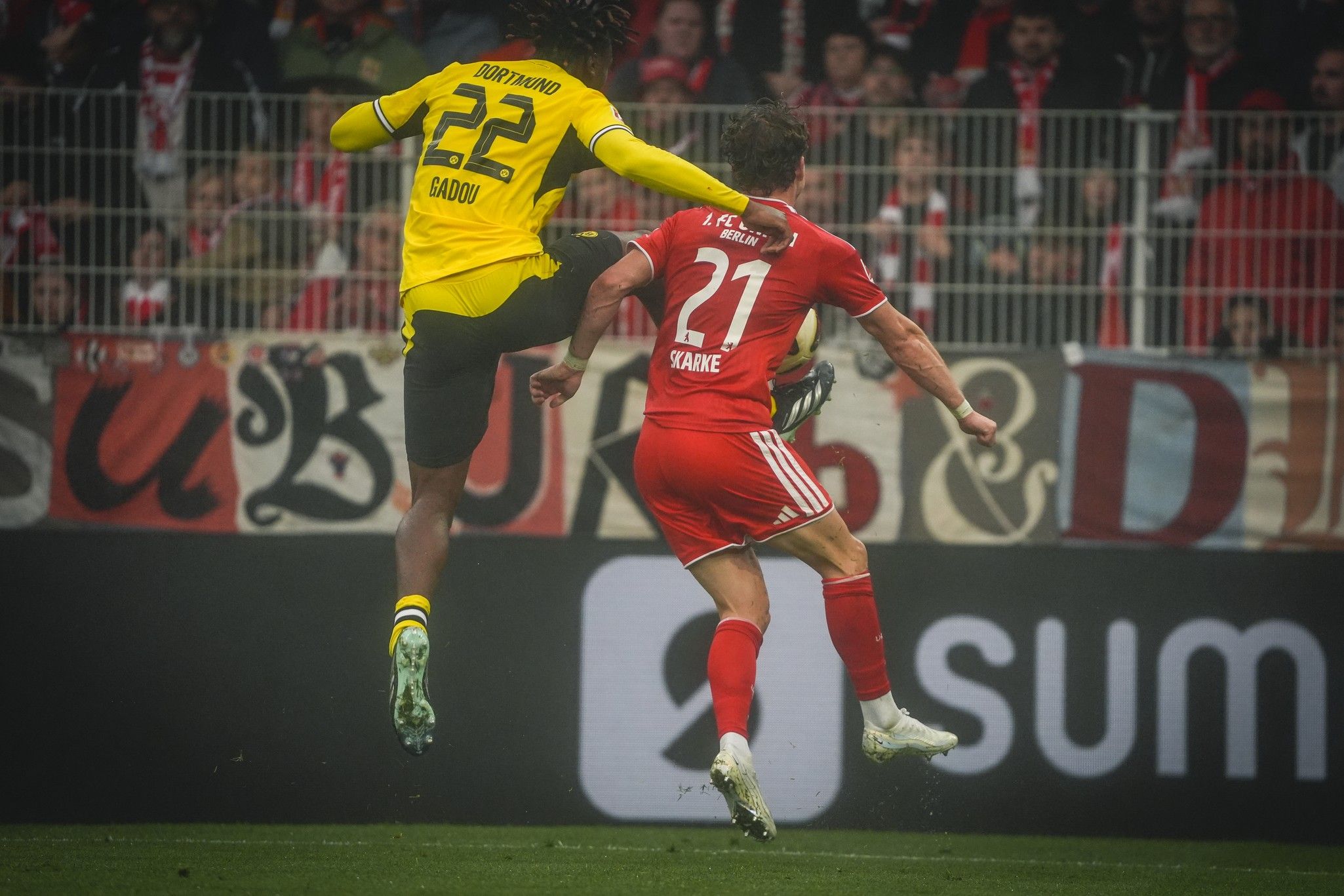 Ein Fußballspieler springt in einem Spiel zum Ball, während ein anderer Spieler dabei ist, ihn zu verteidigen.