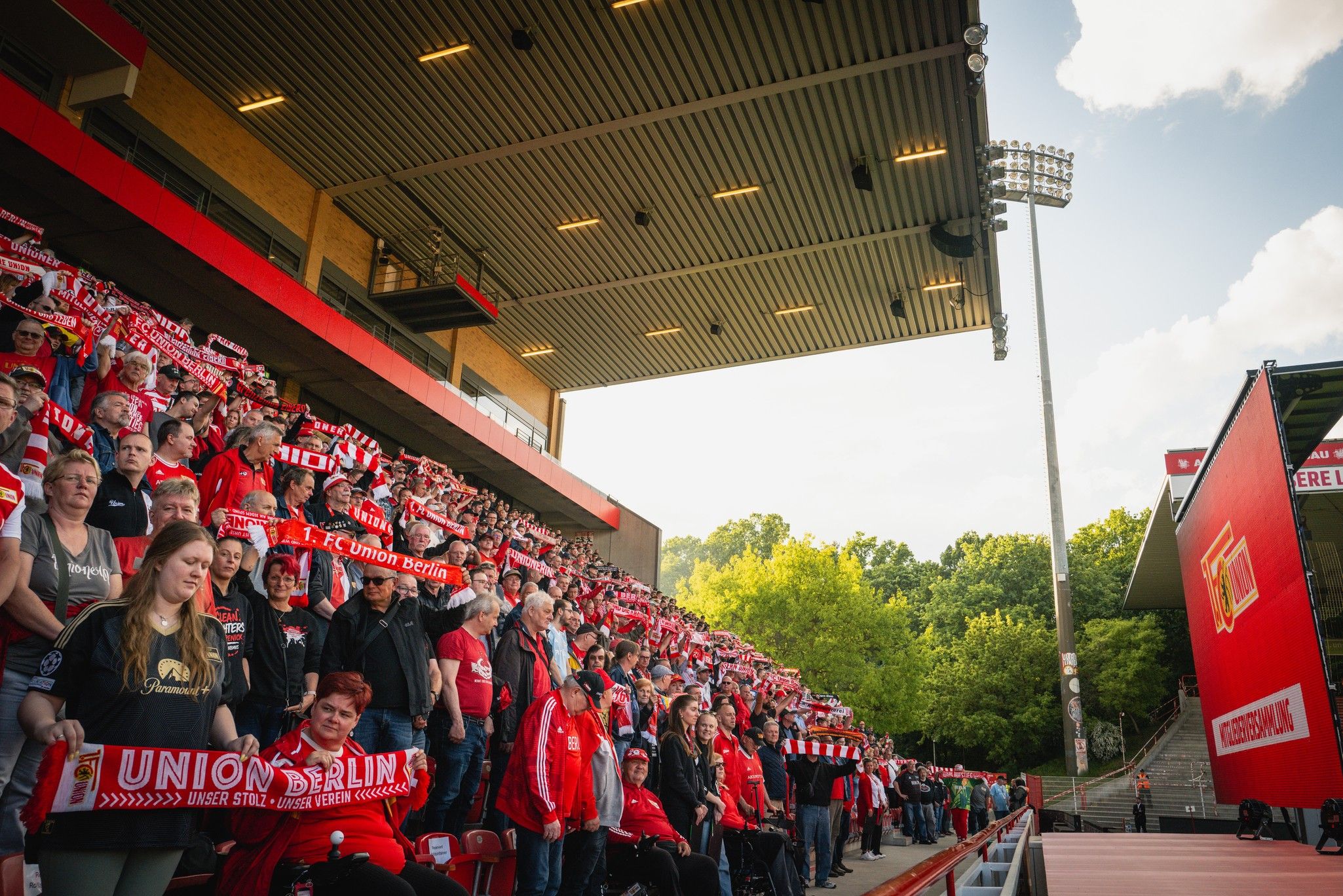 Fans des 1. FC Union Berlin stehen auf den Tribünen, umgeben von roten Schals und einer festlichen Atmosphäre im Stadion.