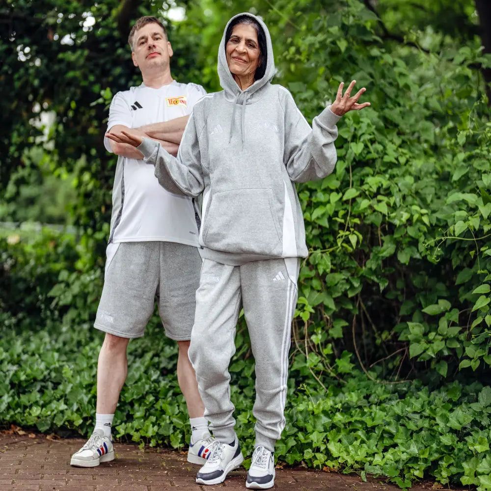 Zwei Personen stehen in Sportkleidung. Sie sind vor einer grünen Landschaft. Sie sehen entspannt aus.