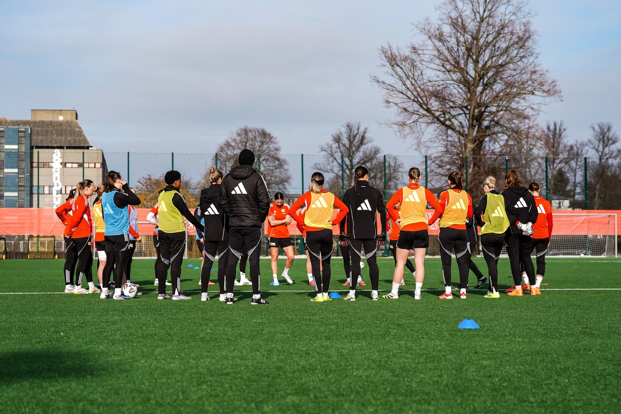 Eine Gruppe von Fußballspielerinnen in Trainingskleidung versammelt sich auf einem grünen Rasenplatz zu einem Training.