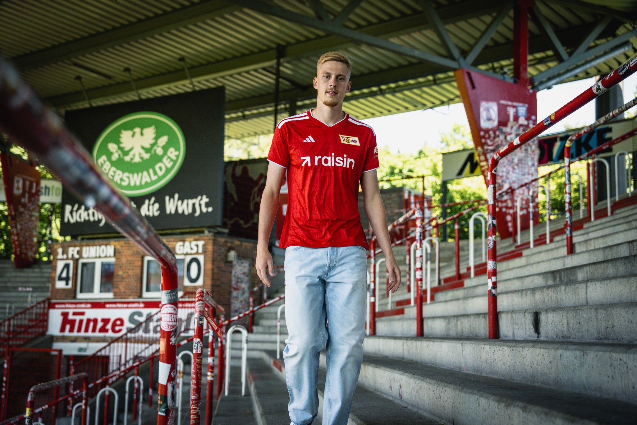 Ein junger Mann im roten Fußballtrikot geht die Treppen in einem Stadion hinunter.