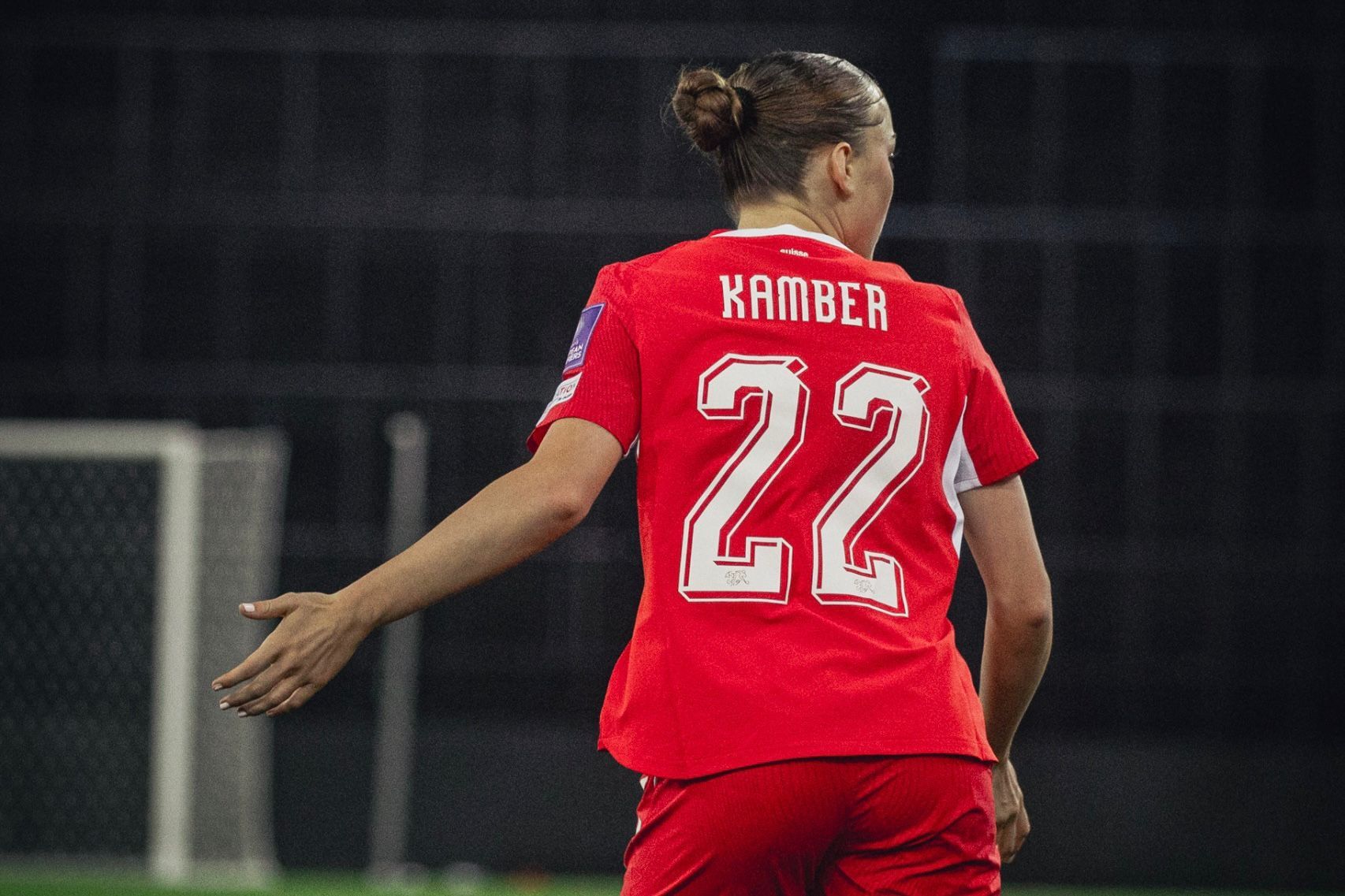 Eine Spielerin in rotem Trikot mit der Nummer 22 und dem Namen "Kamber" steht auf einem Fußballfeld.