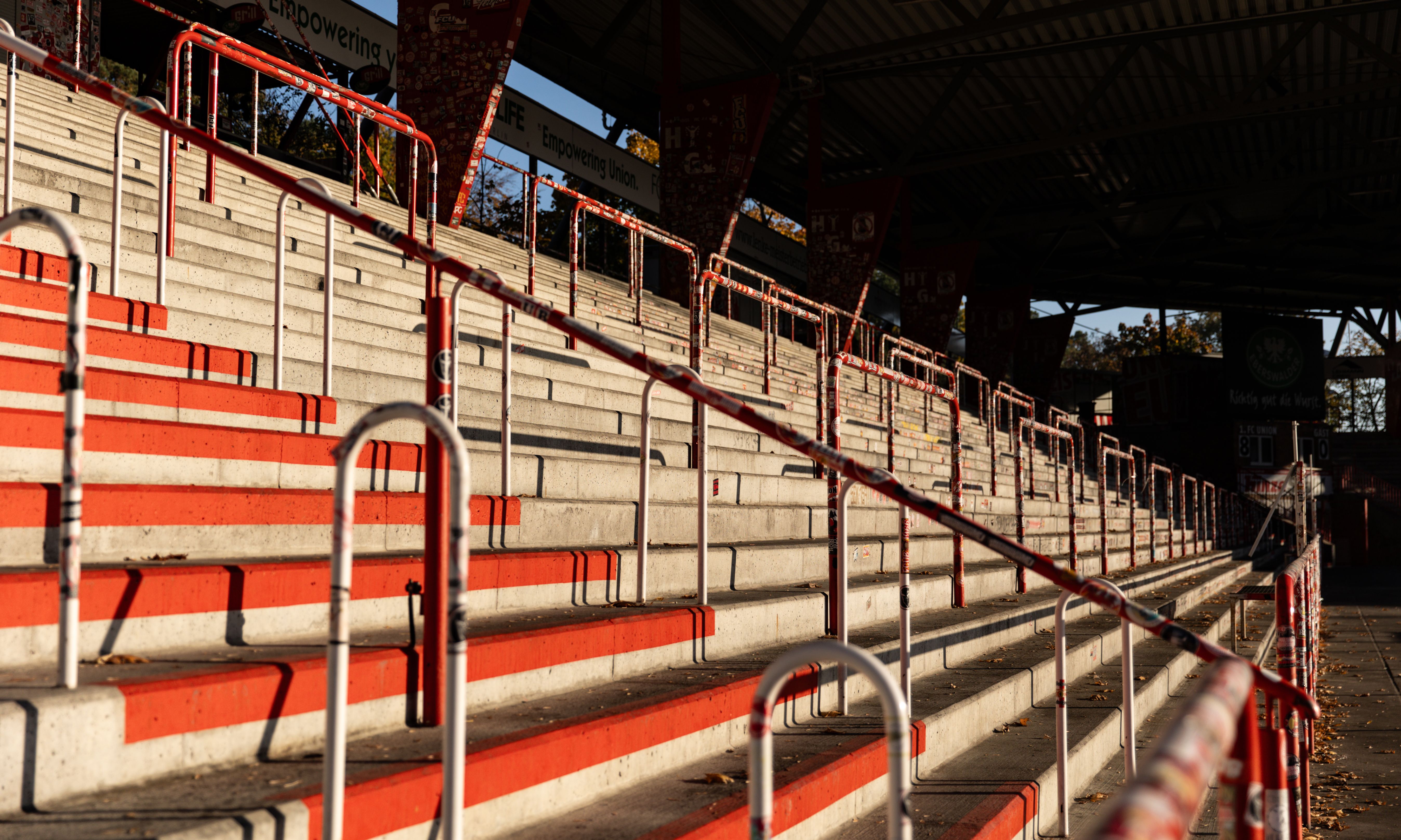 Stufen einer Sporttribüne mit roten und weißen Elementen, teils beleuchtet von der Sonne.