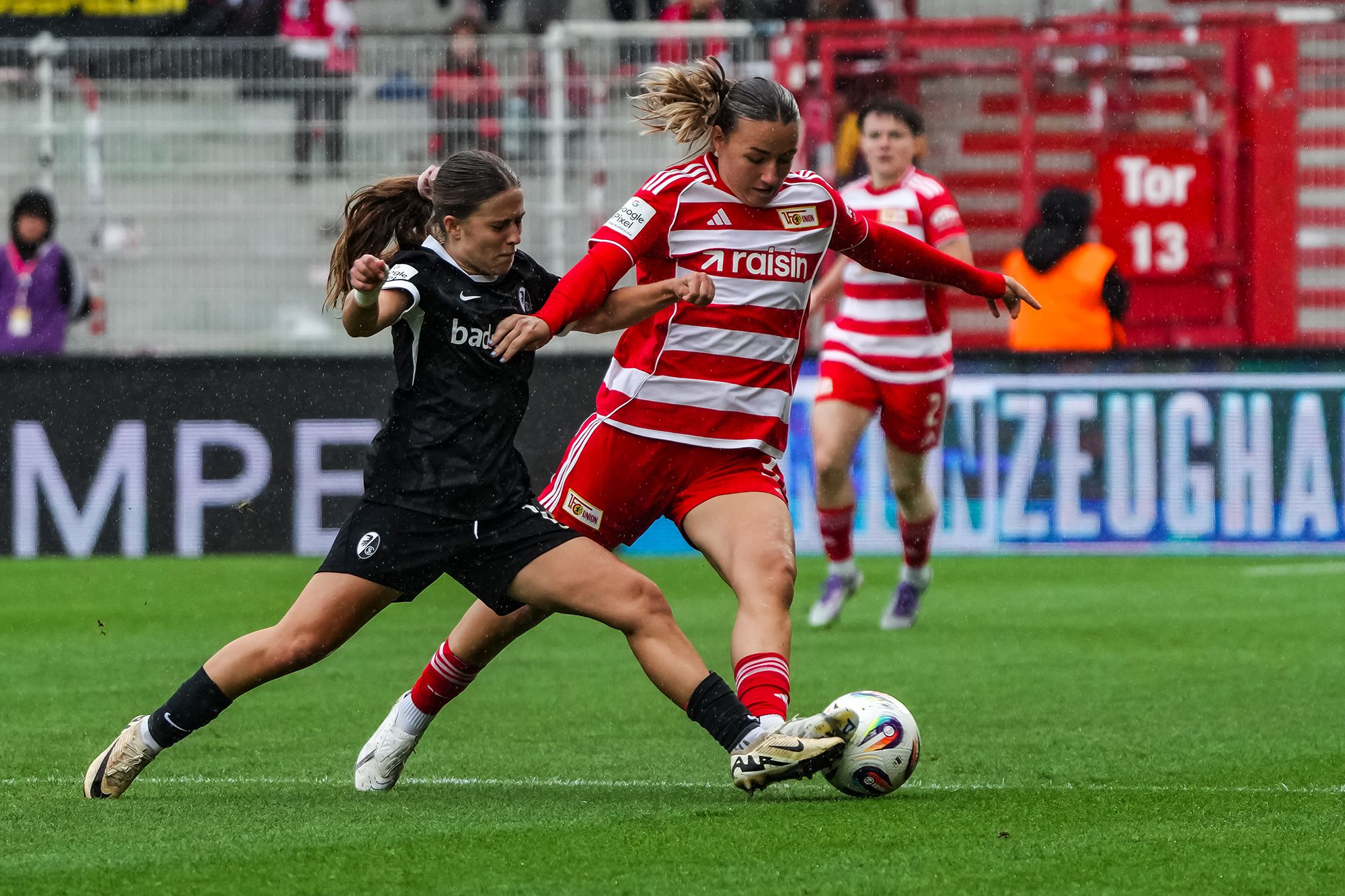 Zwei Fußballspielerinnen in einem Wettkampf um den Ball, eine in roter, die andere in schwarzer Uniform.