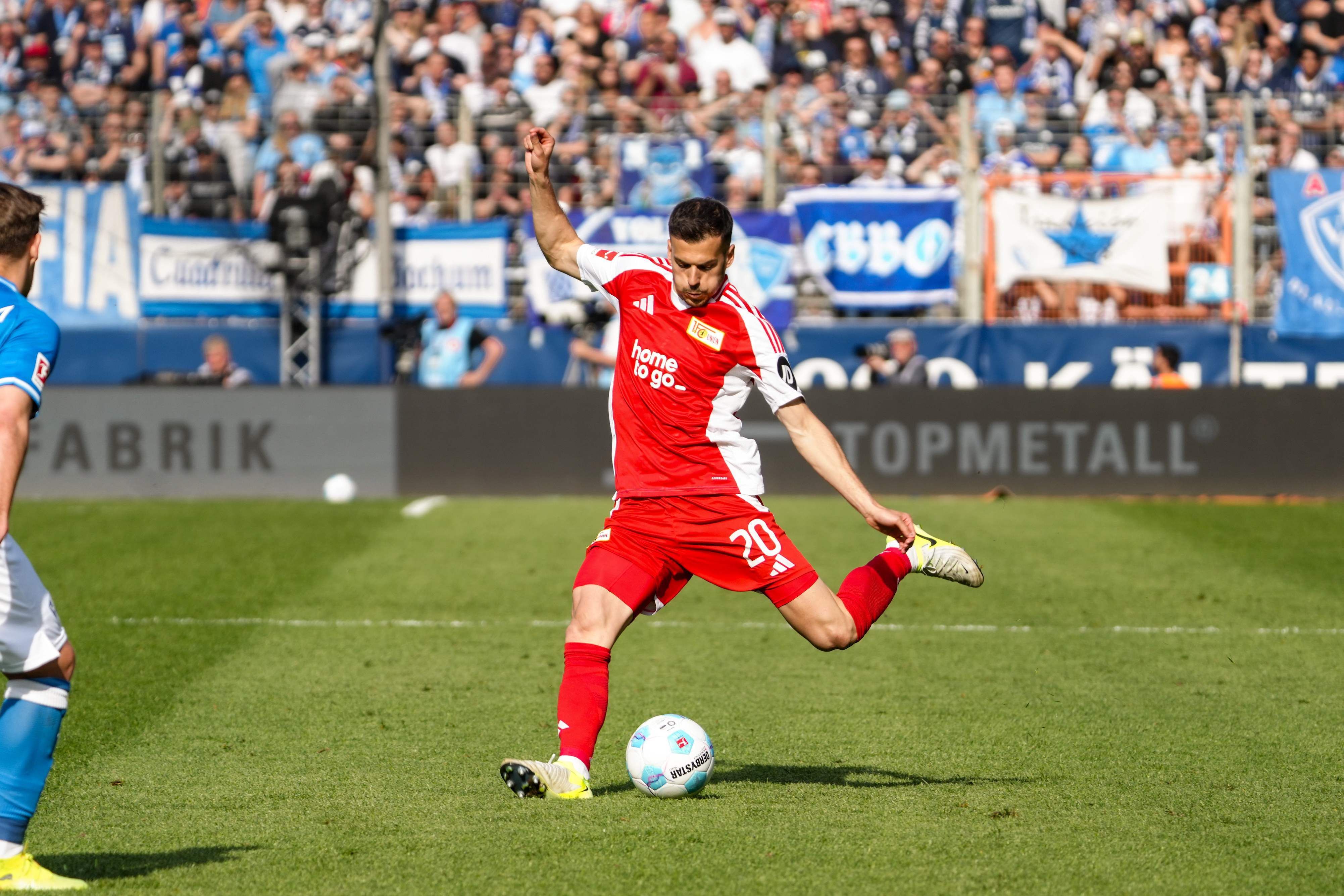Ein Fußballspieler in roter und weißer Uniform tritt den Ball auf einem Rasenplatz während eines Spiels.