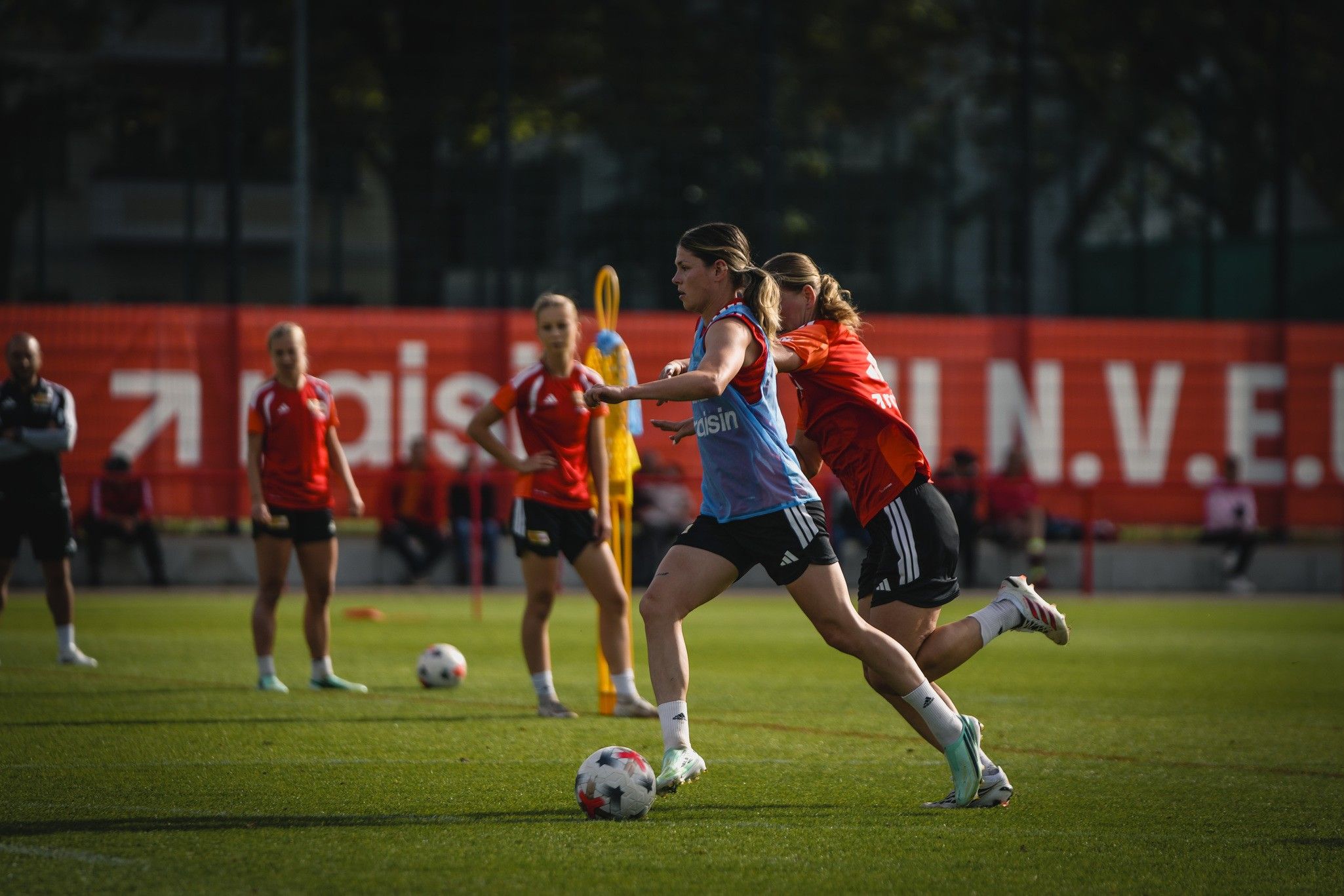 Eine Spielerin in blauer Trikots dribbelt den Ball, während eine andere Spielerin in rotem Trikot sie von hinten anvisiert.
