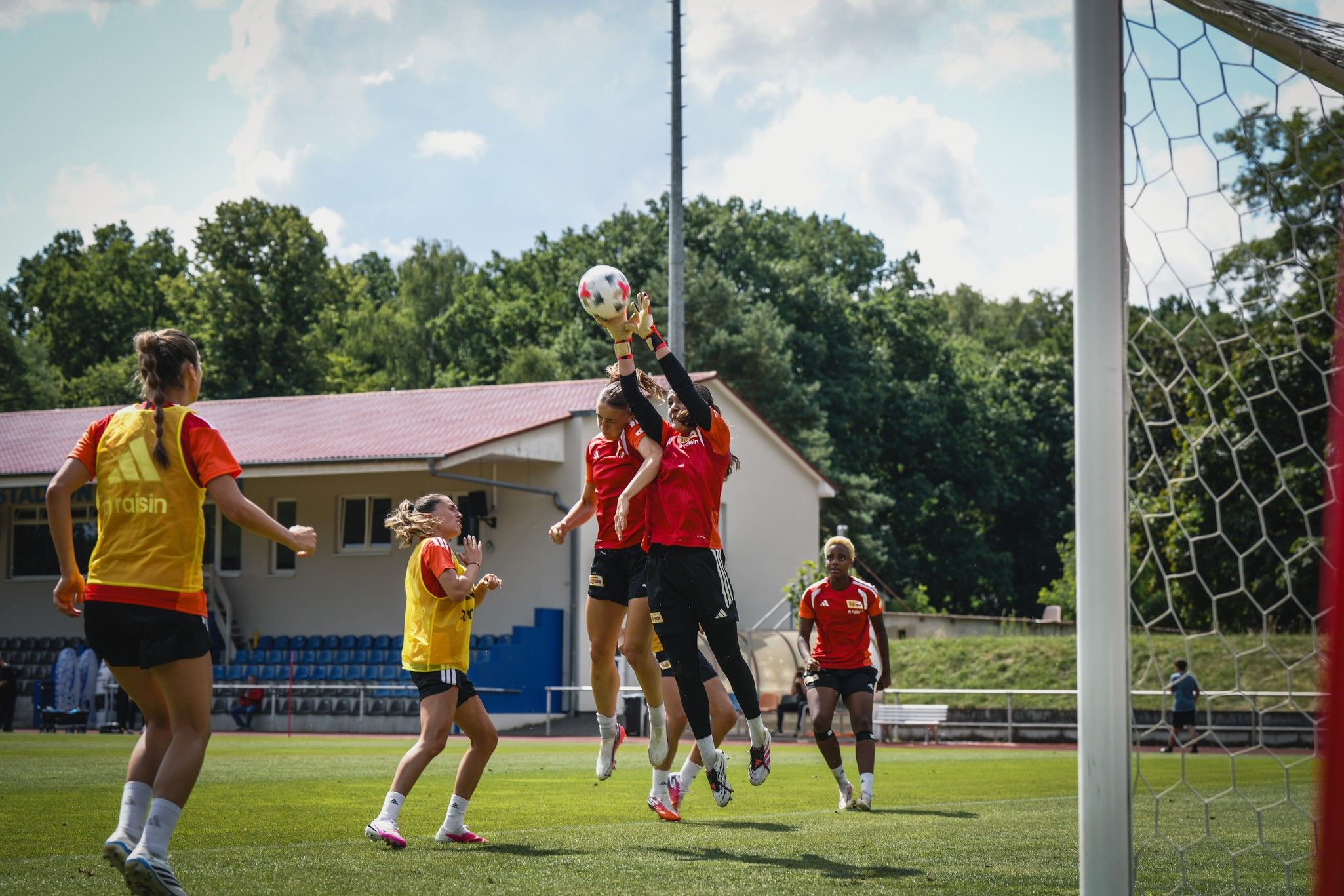 Eine Torhüterin fängt einen Ball während eines Fußballtrainings, umgeben von anderen Spielerinnen auf dem Feld.