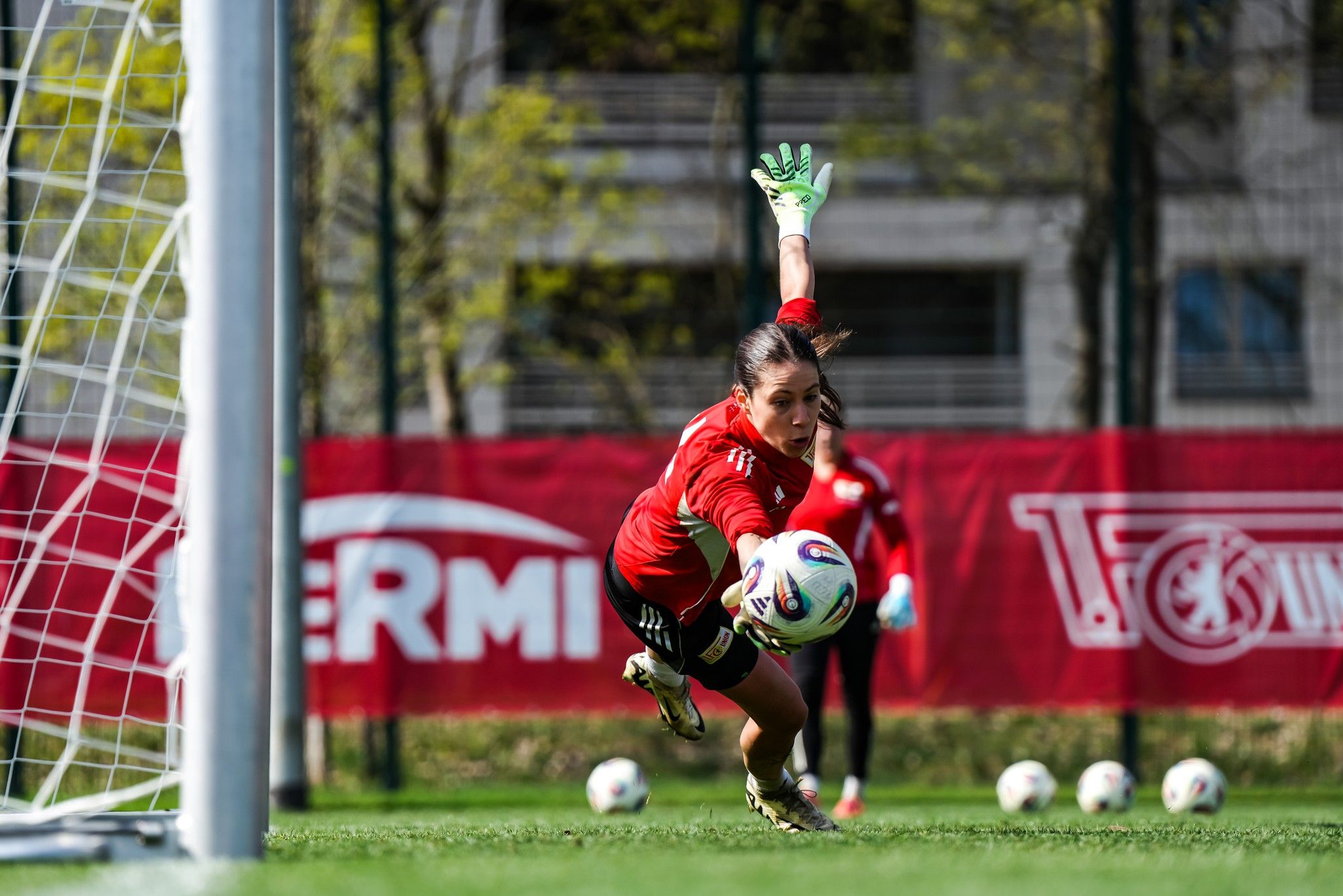 Frau in rotem Trikot springt nach einem Ball während eines Fußballtrainings vor einem Tor.