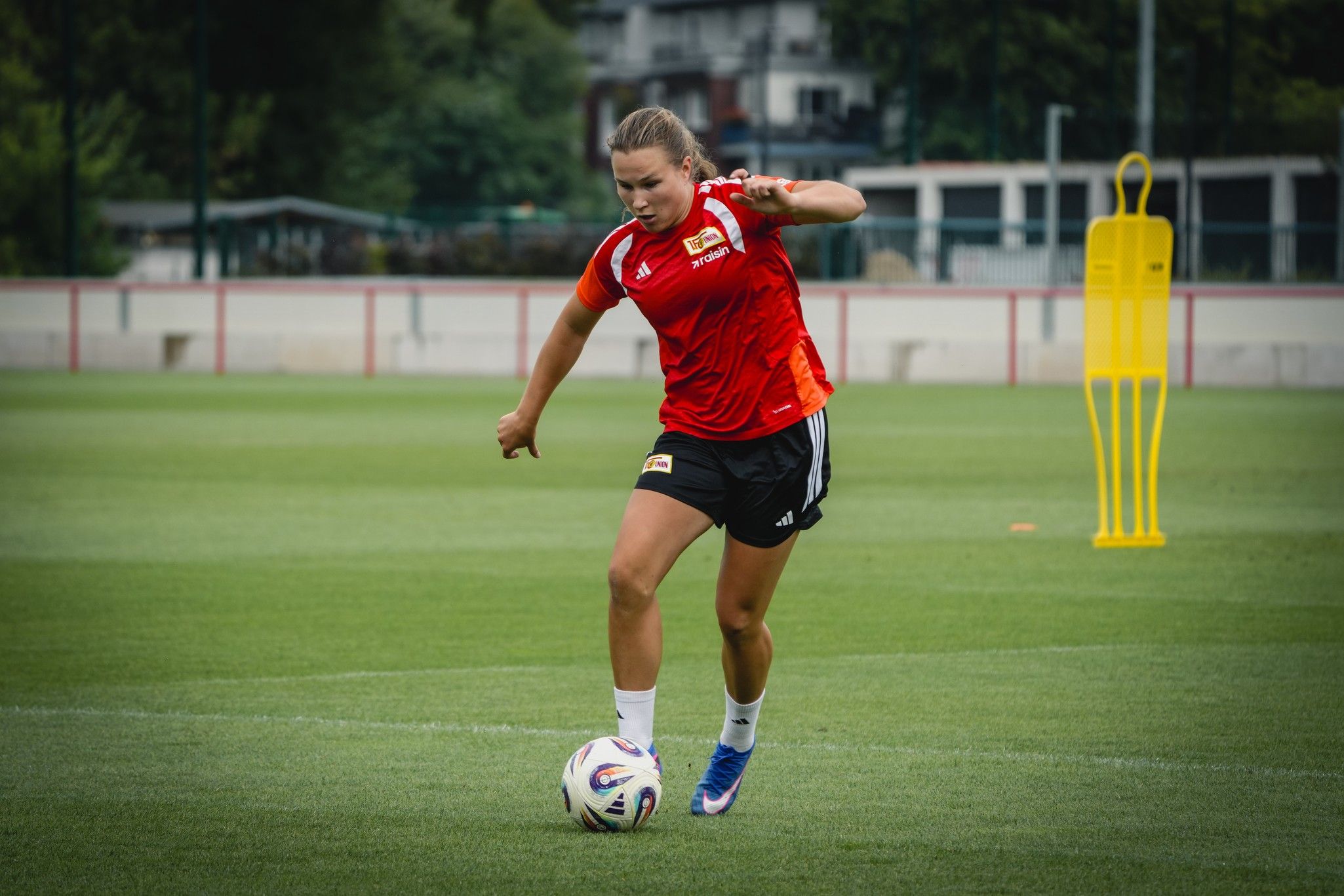 Eine Fußballspielerin in rotem Trikot dribbelt den Ball auf einem grünen Trainingsfeld.