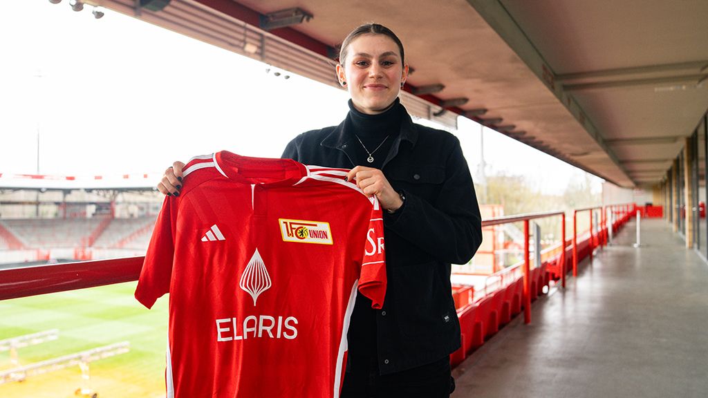 Eine Person hält ein rotes Fußballtrikot mit dem Logo von Union Berlin in einem Stadion.