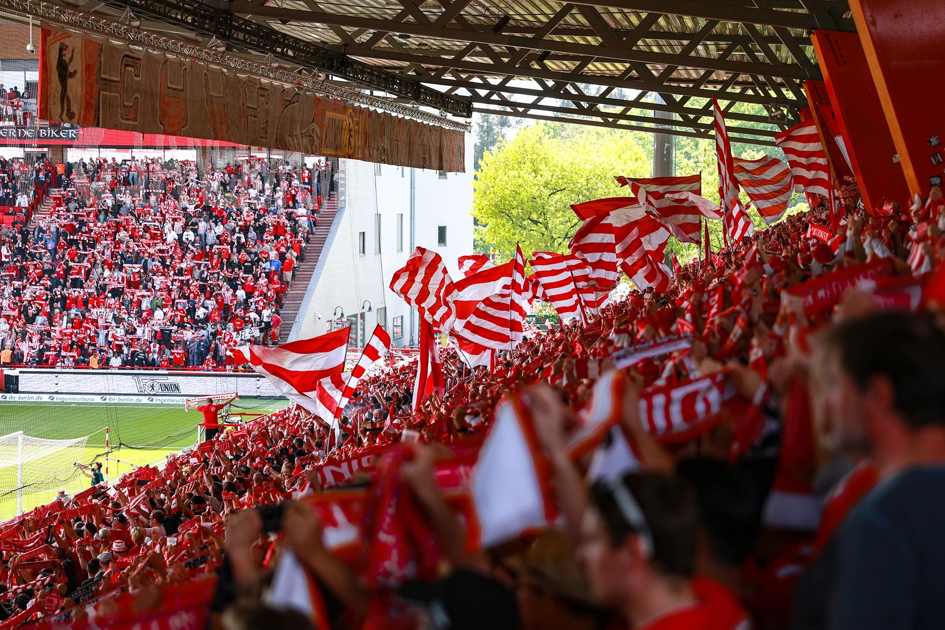 Fans in roten und weißen Trikots schwenken Flaggen und feiern in einem Stadion voller Menschen.