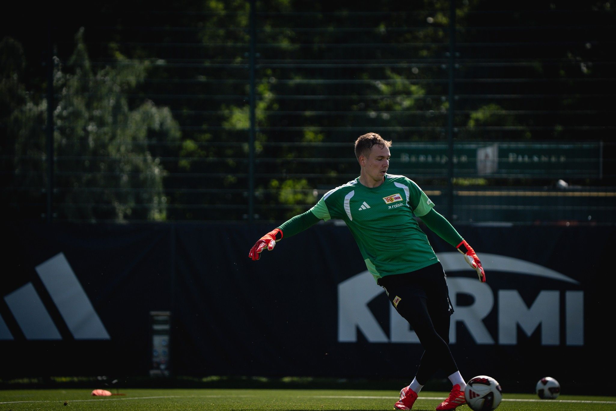 Ein Torwart in grünem Trikot trainiert auf einem Fußballfeld mit Ball.
