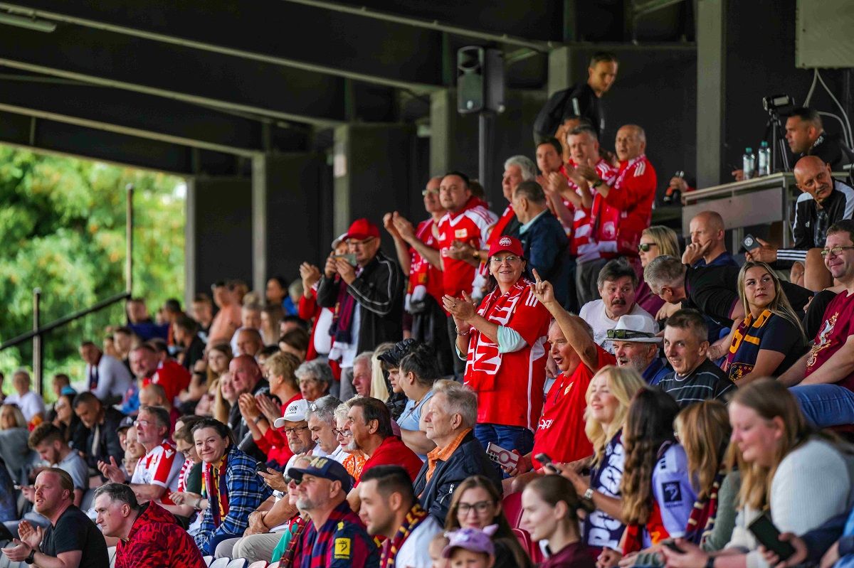 Menschenmenge in roten Trikots und Schals, die in einem Stadion jubeln und applaudieren.