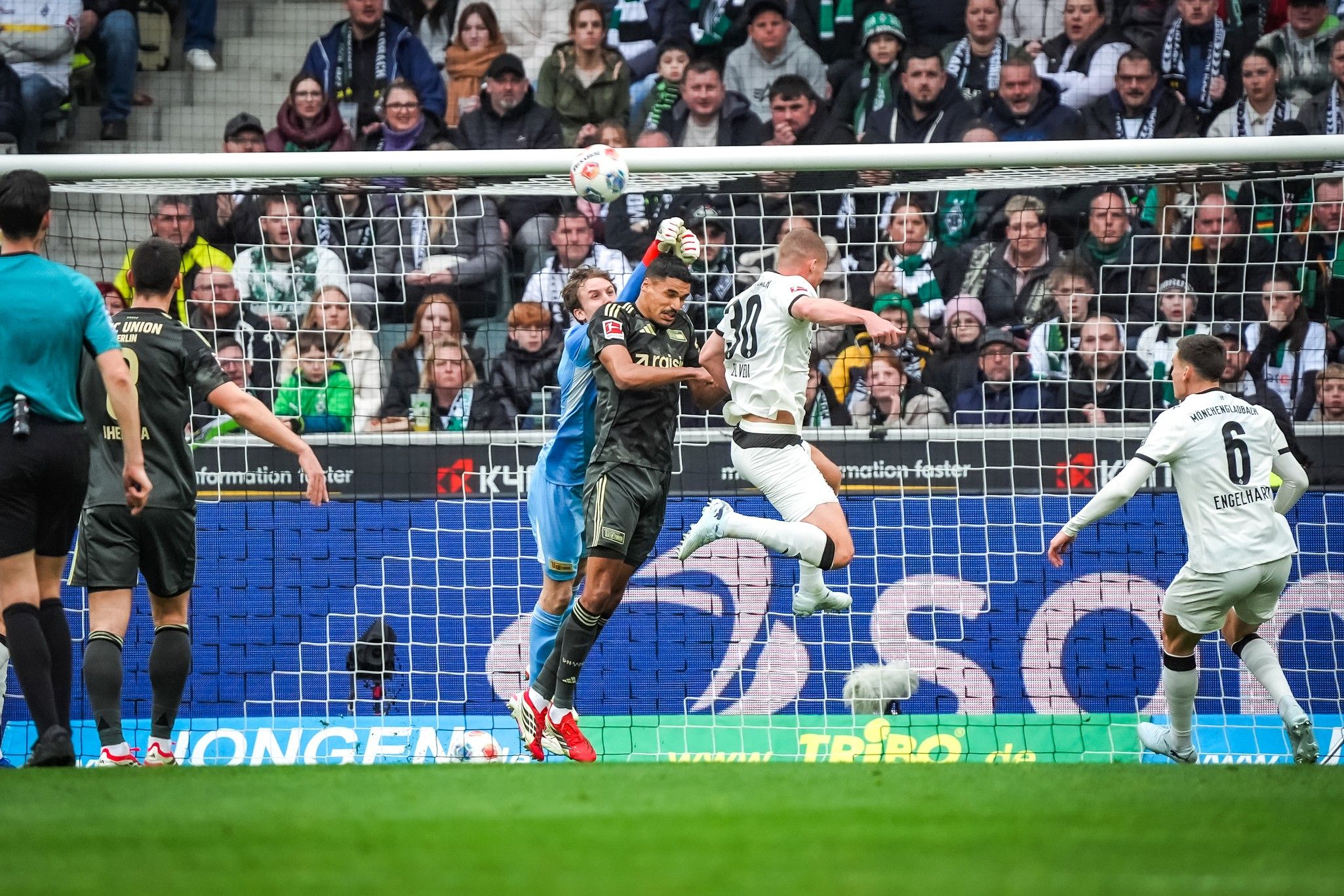 Torwart fängt den Ball in einem Fußballspiel, während Spieler um ihn herum agieren. Zuschauer im Hintergrund.