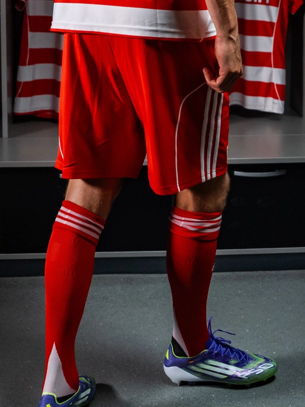 Ein Spieler in rot-weißer Fußballausrüstung steht in einem Umkleideraum, während er auf seine Füße blickt.