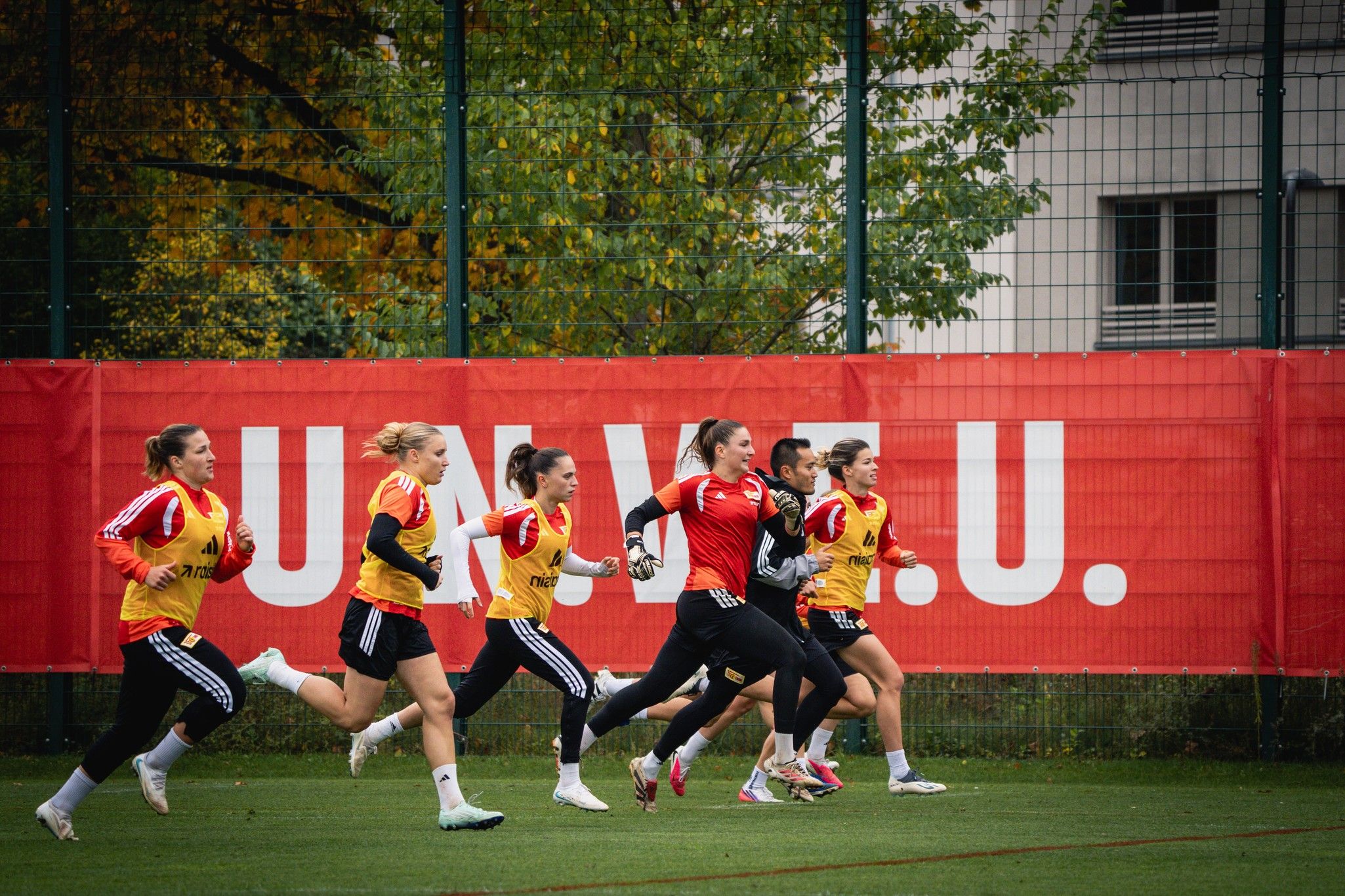 Sechs weibliche Fußballspielerinnen sprinten auf einem Trainingsplatz, während sie Trikots in verschiedenen Farben tragen.
