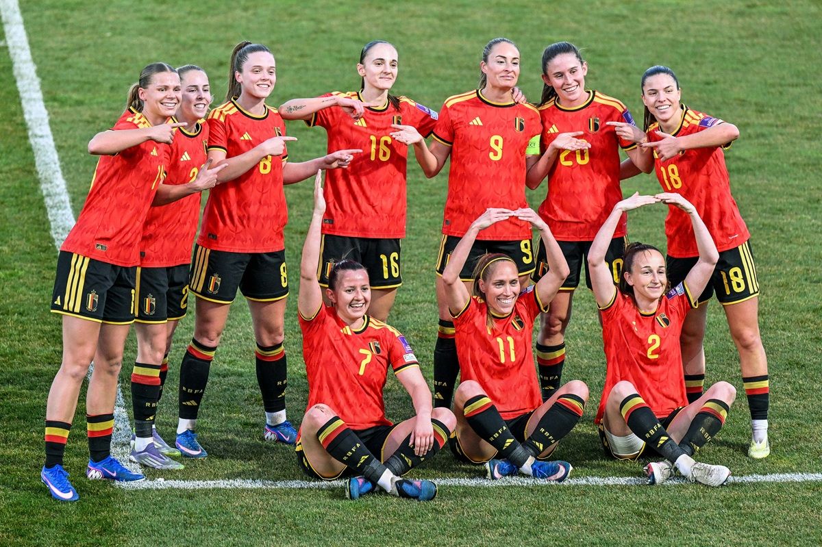 Eine Gruppe von zehn weiblichen Fußballspielerinnen in roten Trikots posiert fröhlich auf dem Spielfeld.
