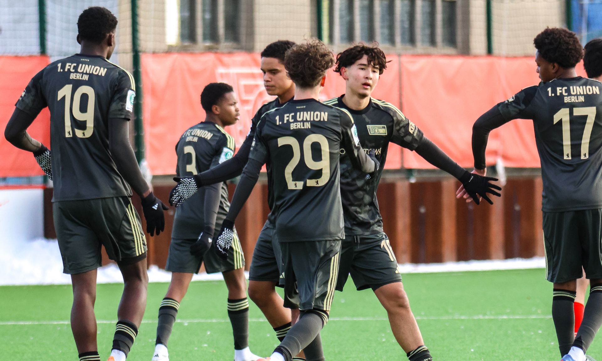 Jugendliche Fußballspieler in schwarzen Trikots stehen auf einem Rasenplatz und feiern ein Tor.