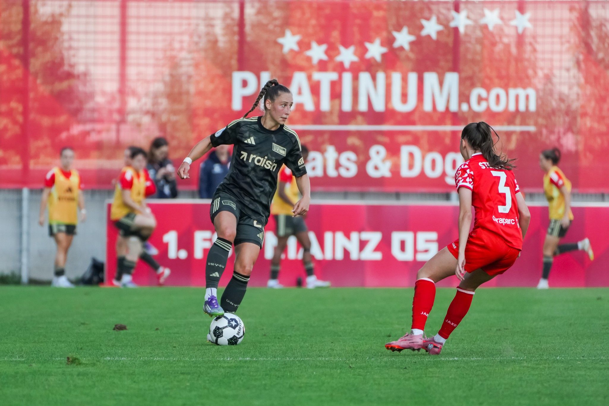 Eine Fußballspielerin mit schwarzer Uniform dribbelt den Ball, während eine andere Spielerin in Rot defensiv positioniert ist.