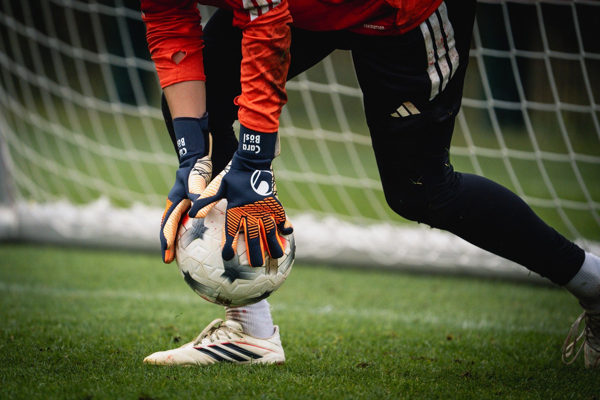 Ein Torwart fängt einen Fußball mit beiden Händen, während er auf einem Rasenfeld vor einem Fußballtor steht.
