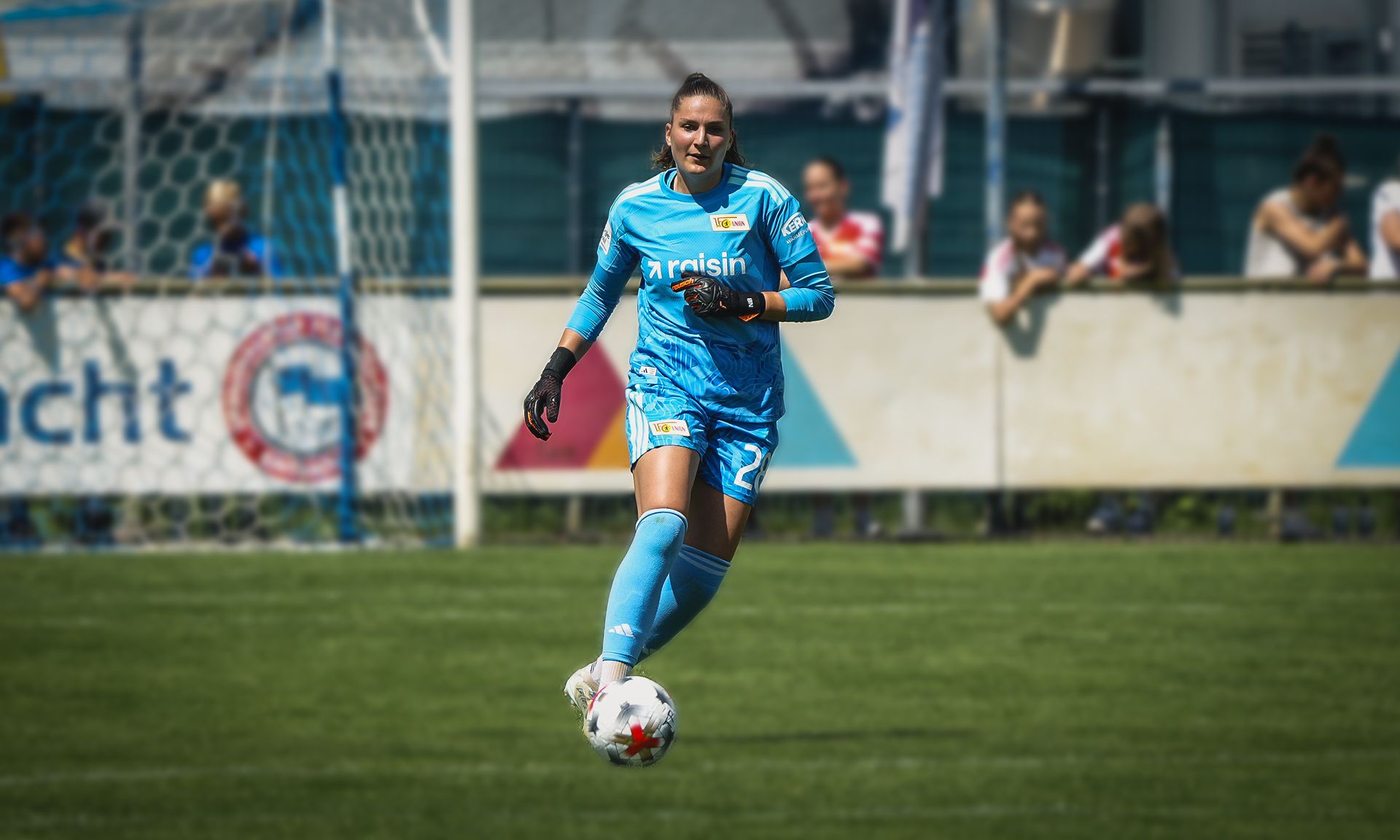 Eine Torhüterin in blauer Sportkleidung spielt auf dem Fußballfeld und bewegt sich zielgerichtet zum Ball.