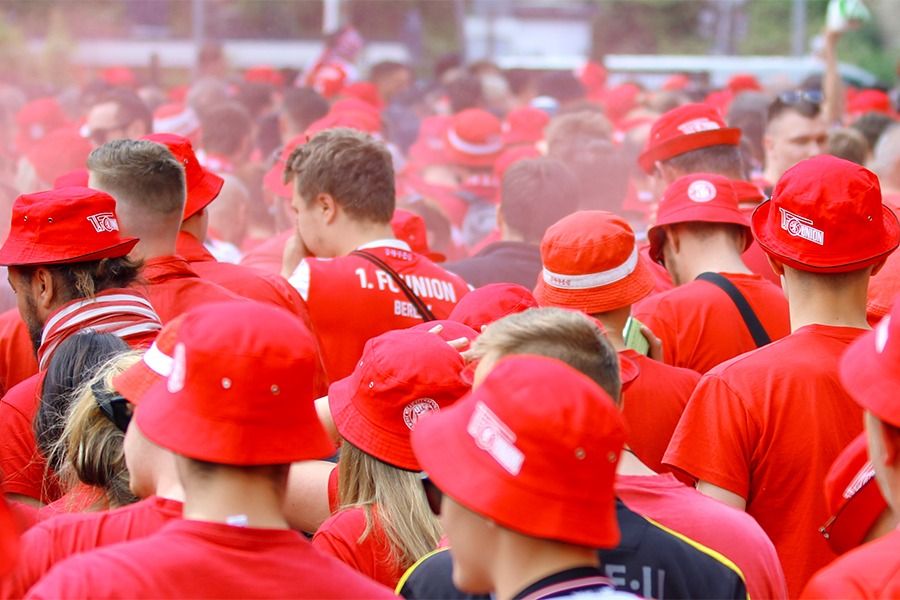 Eine große Menge von Menschen in roten T-Shirts und roten Hüten feiert, umgeben von Rauch und einer festlichen Atmosphäre.