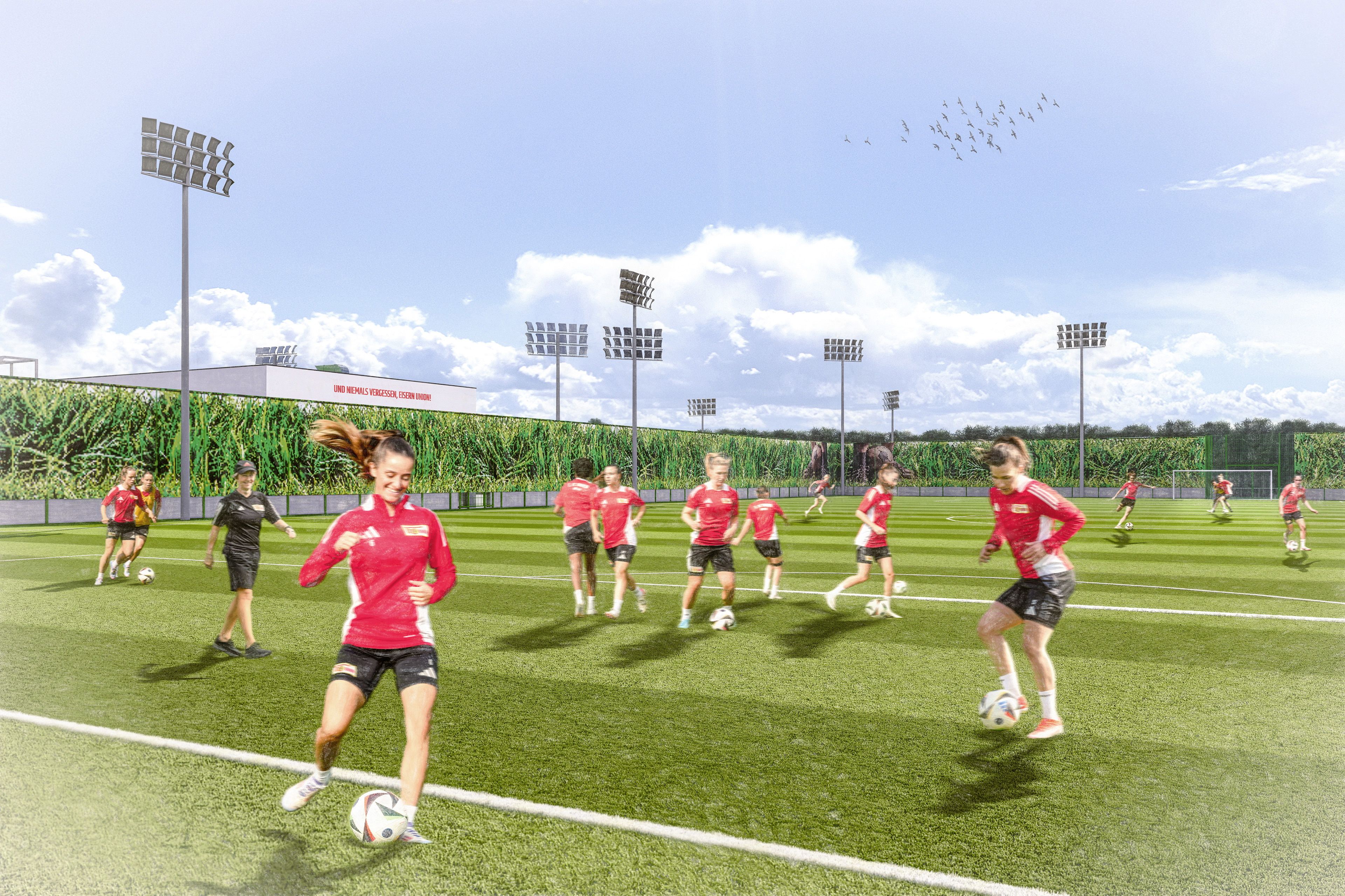 Mannschaft von Frauen in roten Trikots trainiert auf einem Fußballfeld unter blauem Himmel mit Wolken.