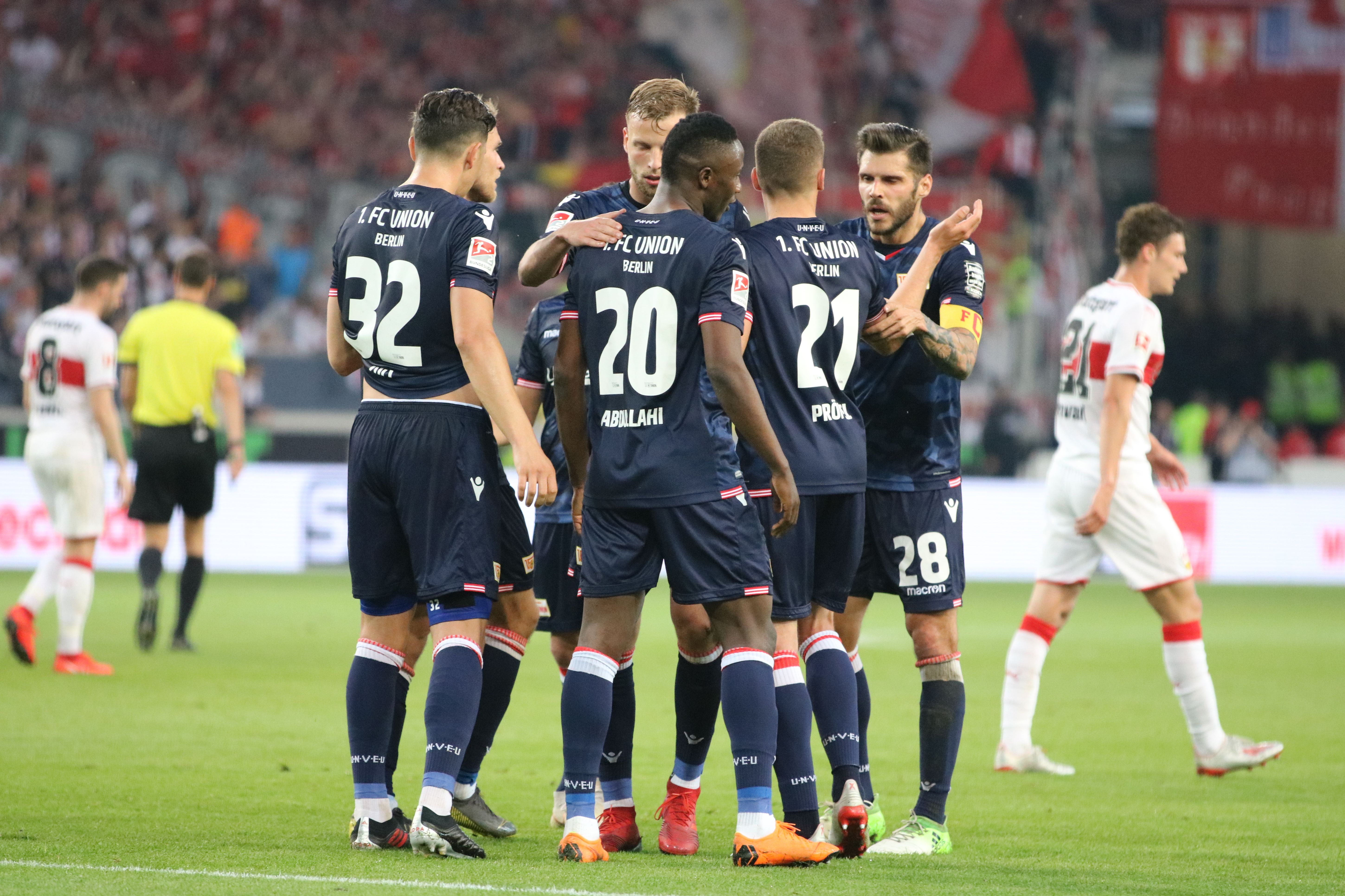 Fußballspieler in blauen Trikots feiern einen Treffer in einem Stadion. Im Hintergrund sind andere Spieler und Zuschauer zu sehen.