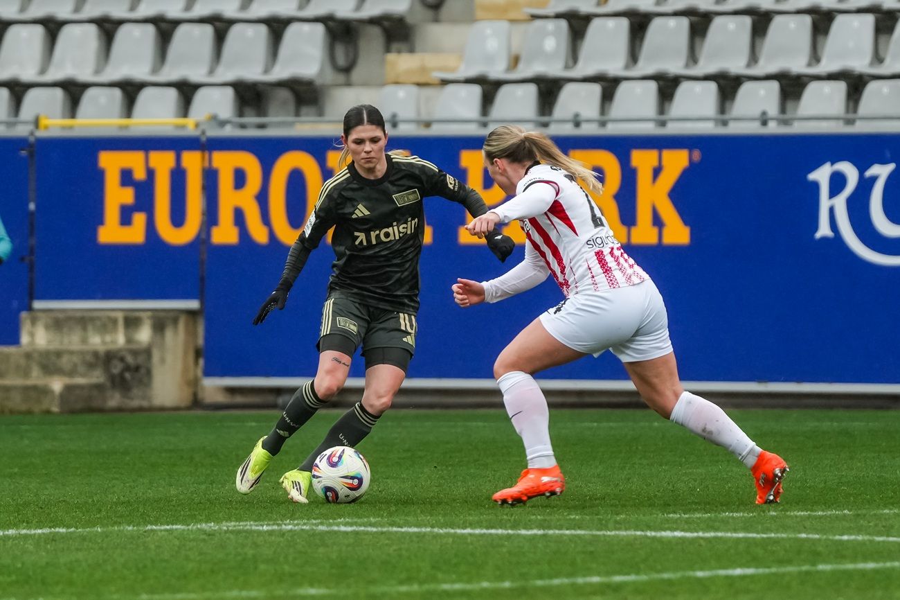 Zwei Fußballspielerinnen im Wettkampf, eine mit Ballführung in schwarzer Ausrüstung, die andere versucht, den Ball zu erobern.