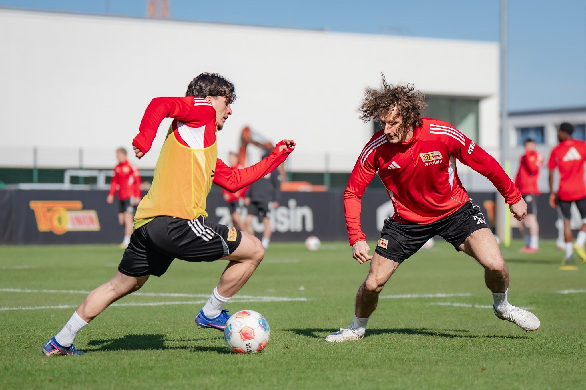Zwei Fußballspieler im Training, die in einem intensiven Sprintduell auf einem grünen Rasenplatz gegeneinander antreten.