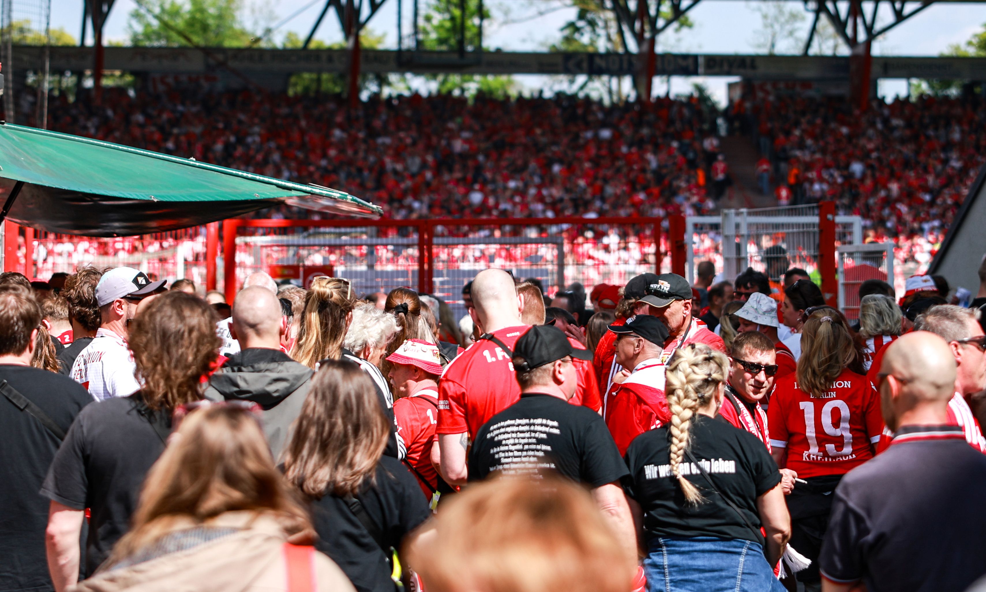 Vieler Menschen in roten Trikots und Fanschals auf einem Stadiongelände, mit Menschenmengen und Atmosphäre eines Spiels.