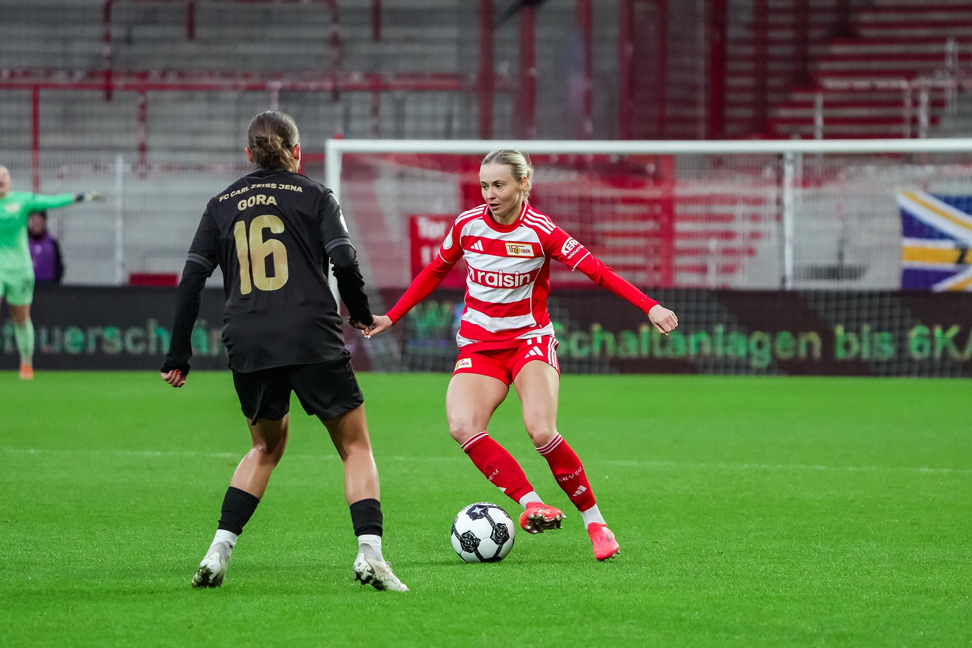 Zwei Fußballspielerinnen in action: Eine in rotem Trikot dribbelt, während die andere in schwarzem auf Verteidigung steht.