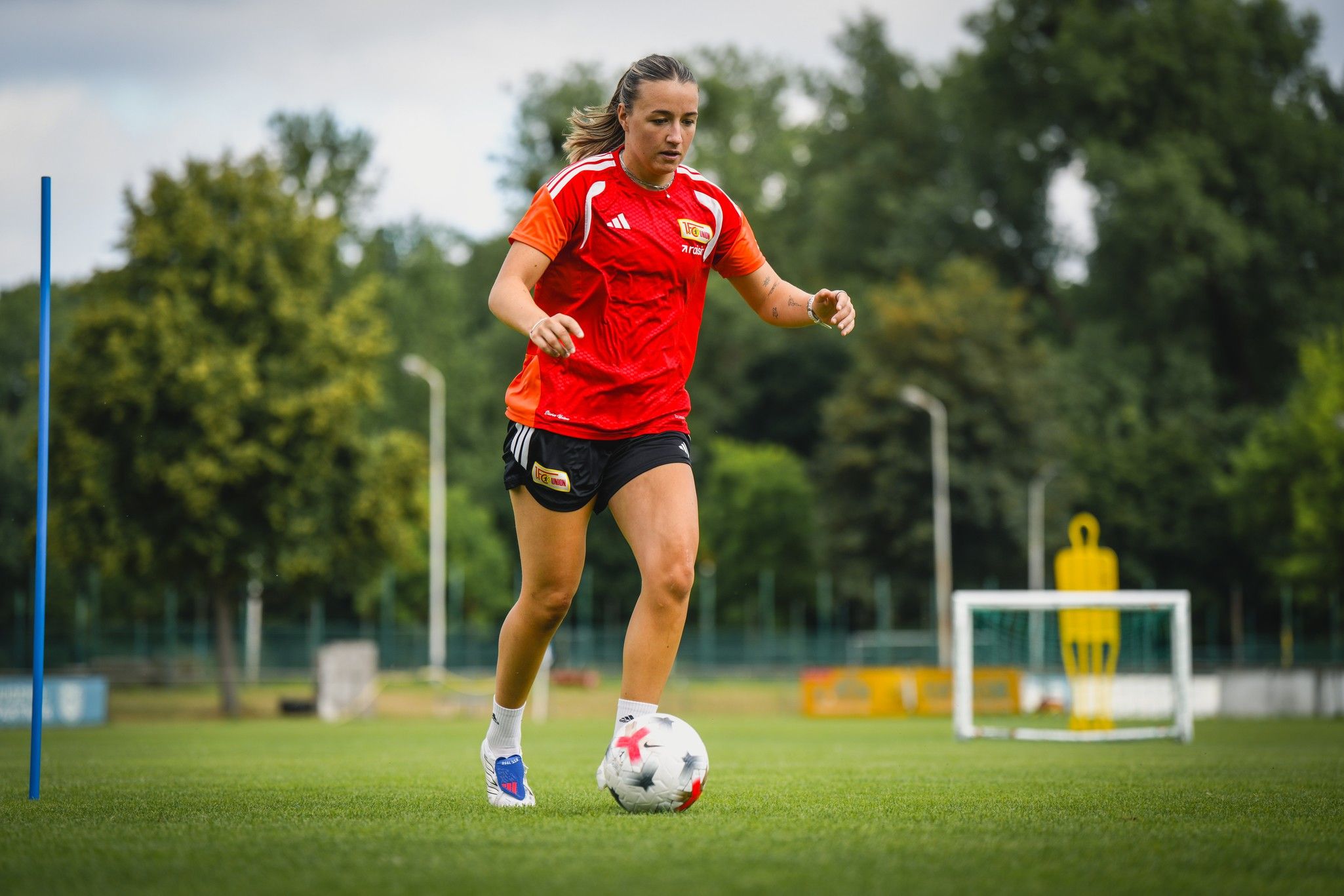 Eine Fußballspielerin trainiert auf dem Spielfeld, umgeben von Trainingshilfen und dem Tor im Hintergrund.